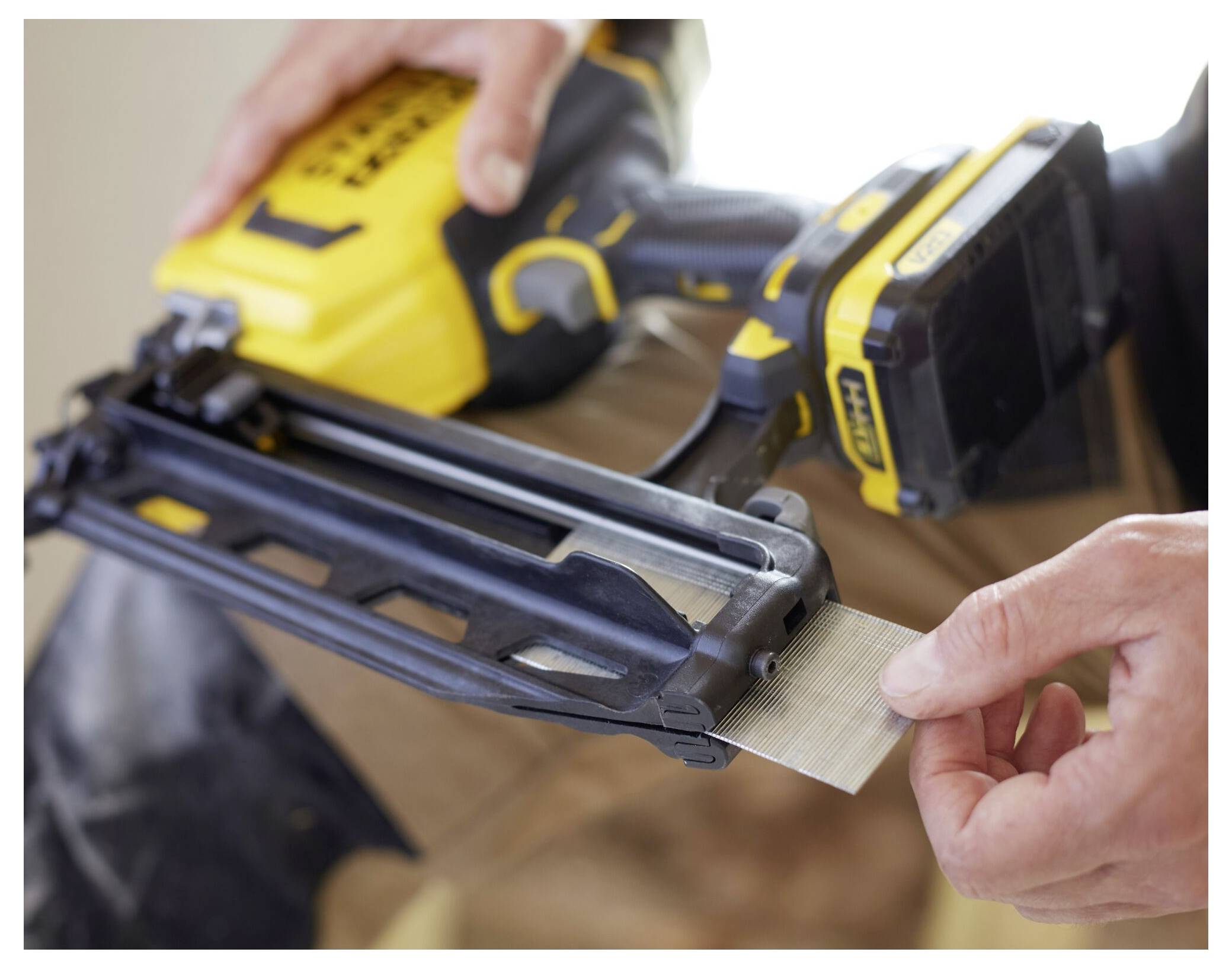 Eine Person führt einen Streifen mit Nägeln in eine gelb-schwarze Nagelspistole ein und bereitet diese für eine Verwendung bei einer Bau- oder Renovierungsaufgabe vor.