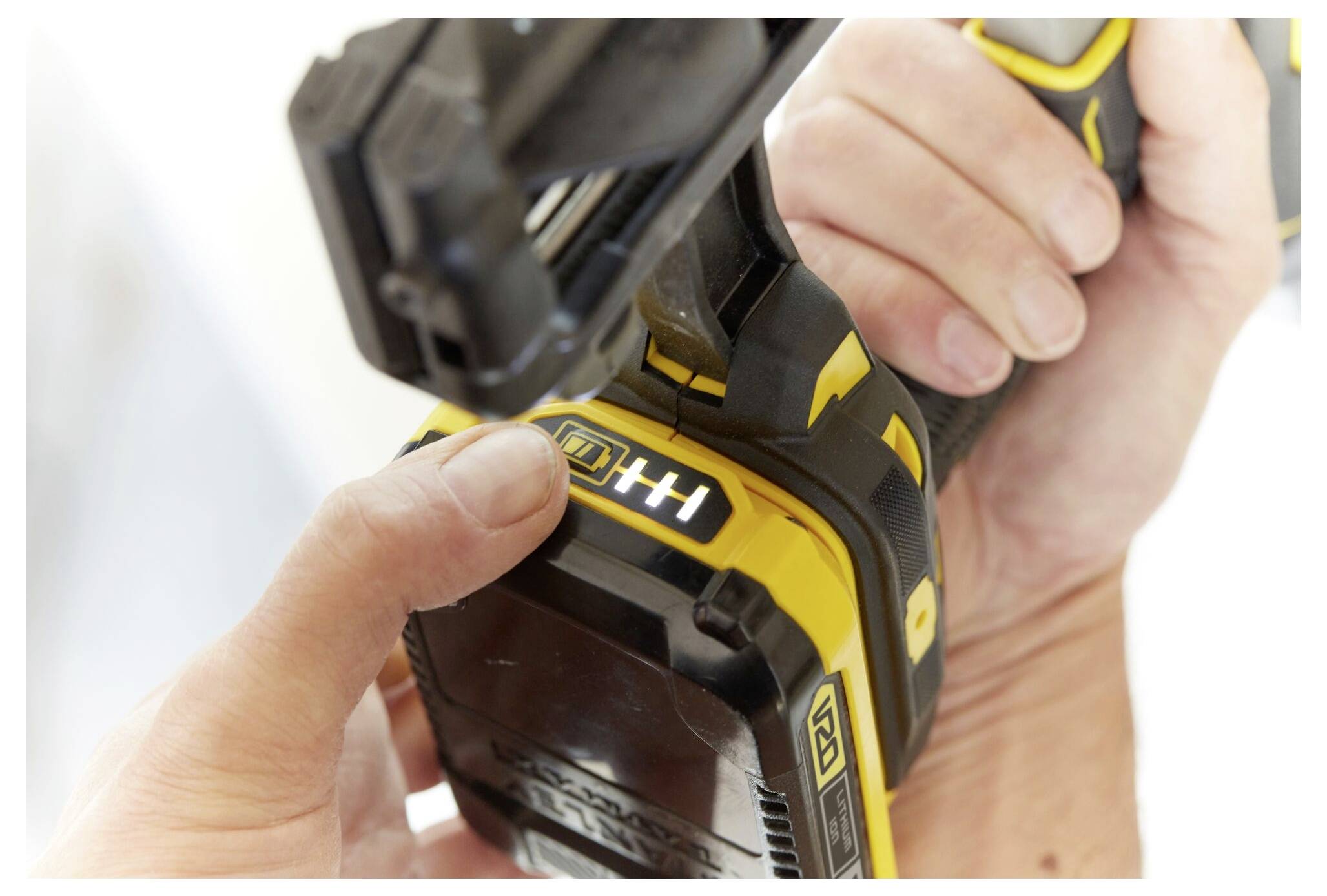 Nahaufnahme einer Person, die einen Akku an einem gelb-schwarzen Elektrowerkzeug wechselt, wobei eine Hand den Akku-Freigabeknopf betätigt.