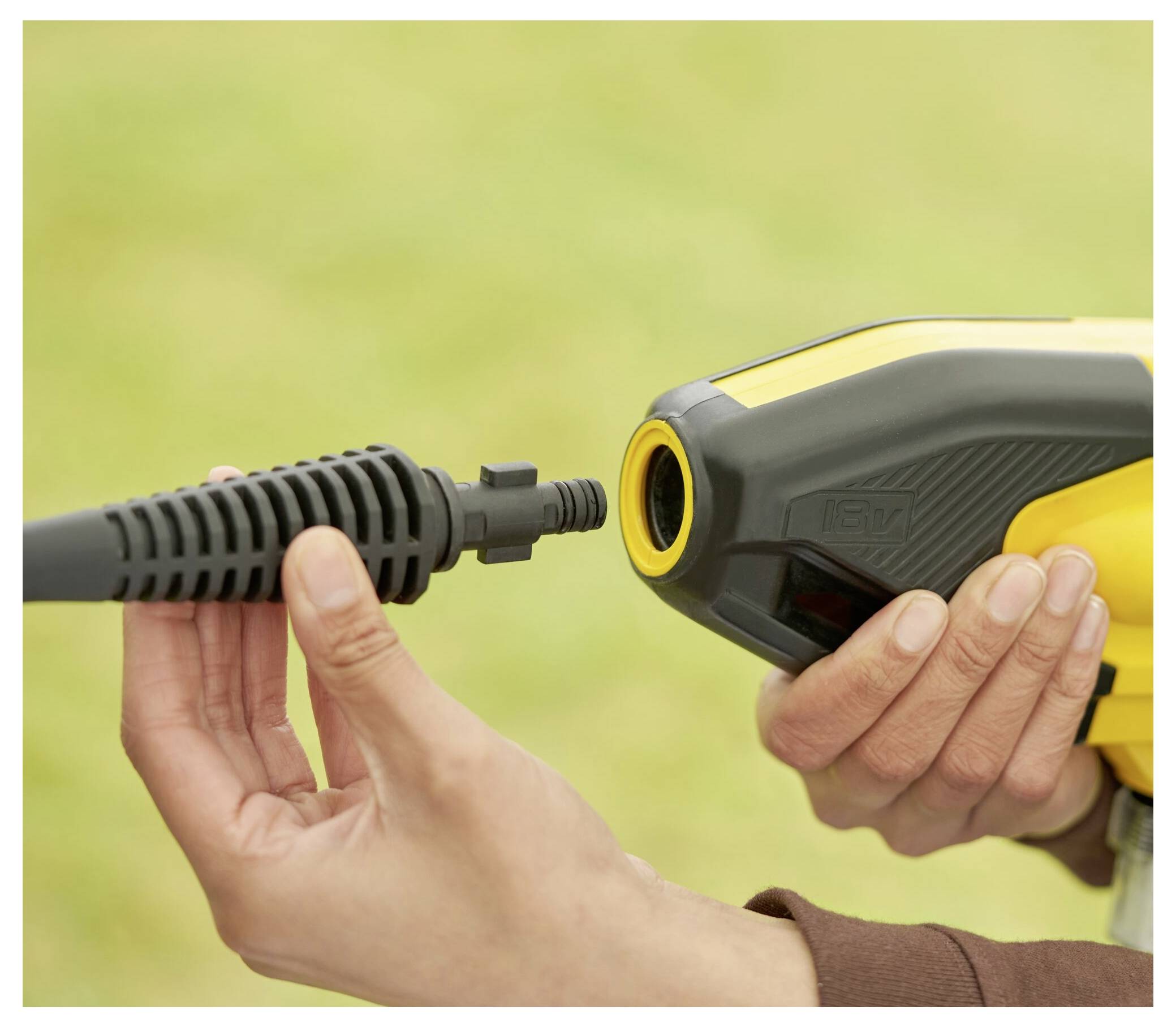 Eine Person verbindet einen Schlauch mit einer gelben Hochdruckreiniger-Düse und demonstriert die Montage. Der Hintergrund ist unscharf, um die Aufgabe hervorzuheben.