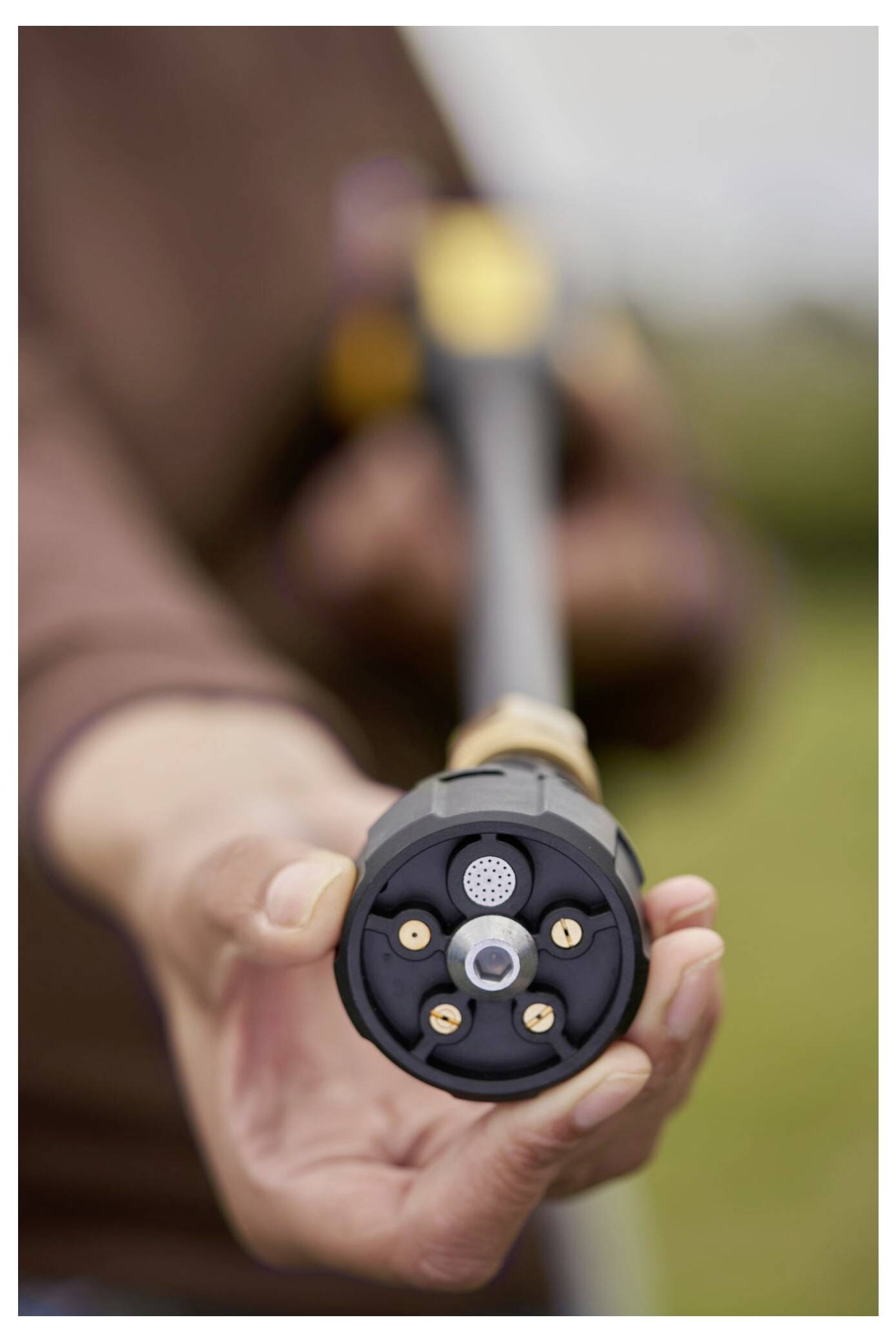 Eine Person hält eine Gartenschlauch-Düse in Richtung der Kamera, die ihre verschiedenen Sprüheinstellungen zeigt. Der Hintergrund ist unscharf.