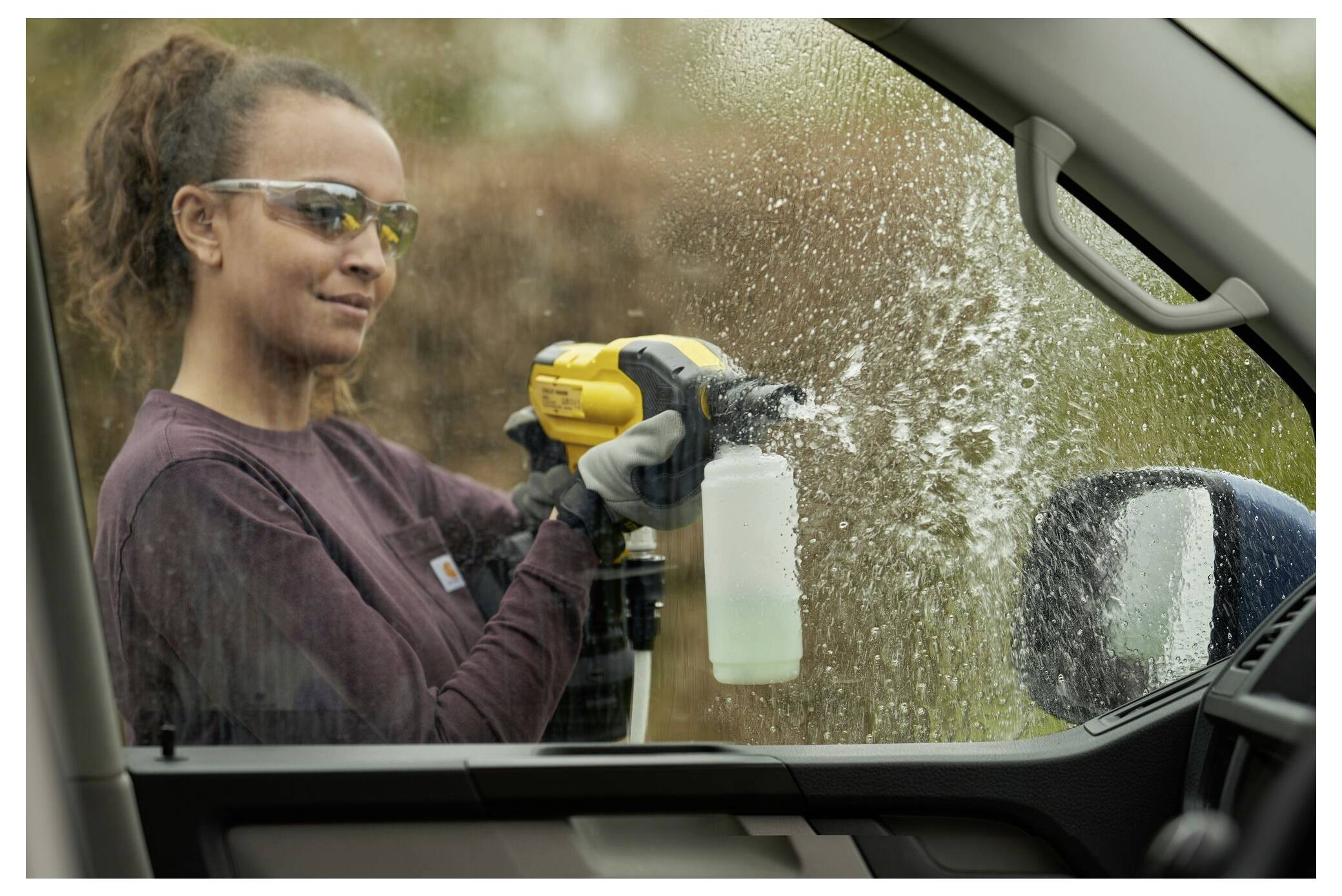 Eine Person, die Schutzbrille und Handschuhe trägt, benutzt ein motorisiertes Sprühgerät, um ein Autofenster von außen zu reinigen.