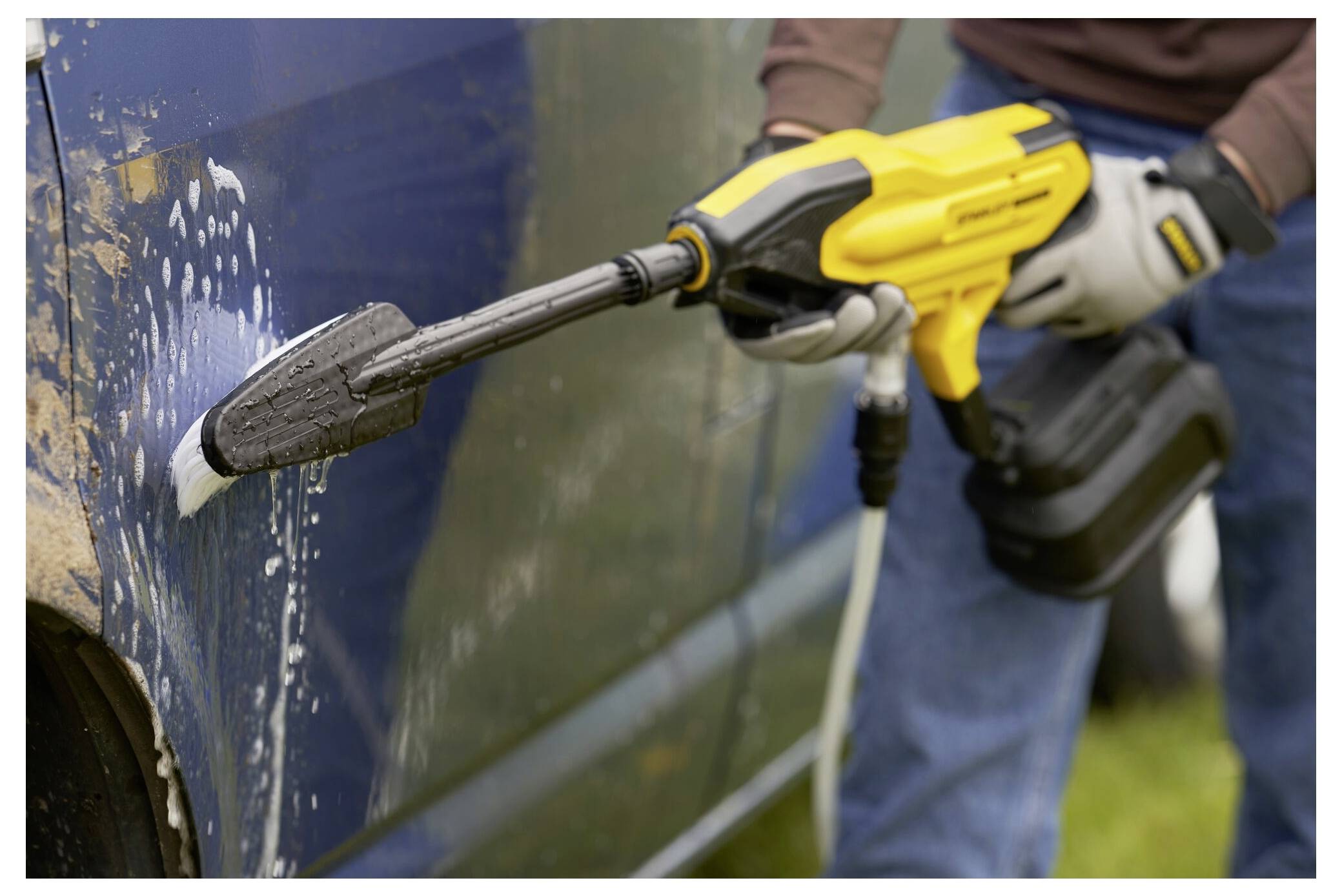 Eine Person benutzt einen gelben Hochdruckreiniger, um die Oberfläche eines blauen Autos zu reinigen und Schmutz sowie Verschmutzungen zu entfernen. Das Auto ist teilweise seifig.