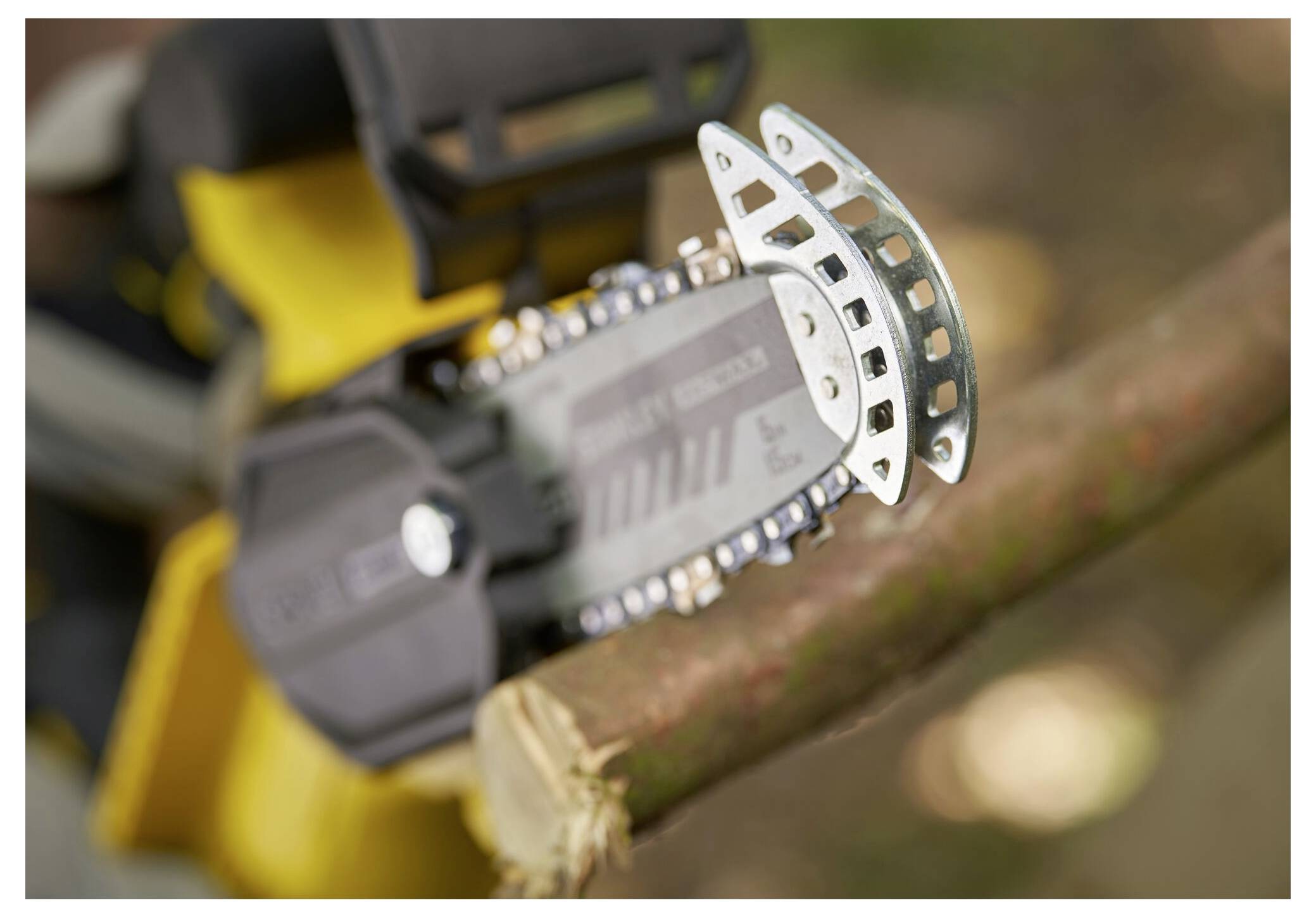 Eine kleine Kettensägenklinge schneidet durch einen Baumast mit unscharfem Hintergrund, wobei die Aktion des Werkzeugs und seine Schärfe hervorgehoben werden.