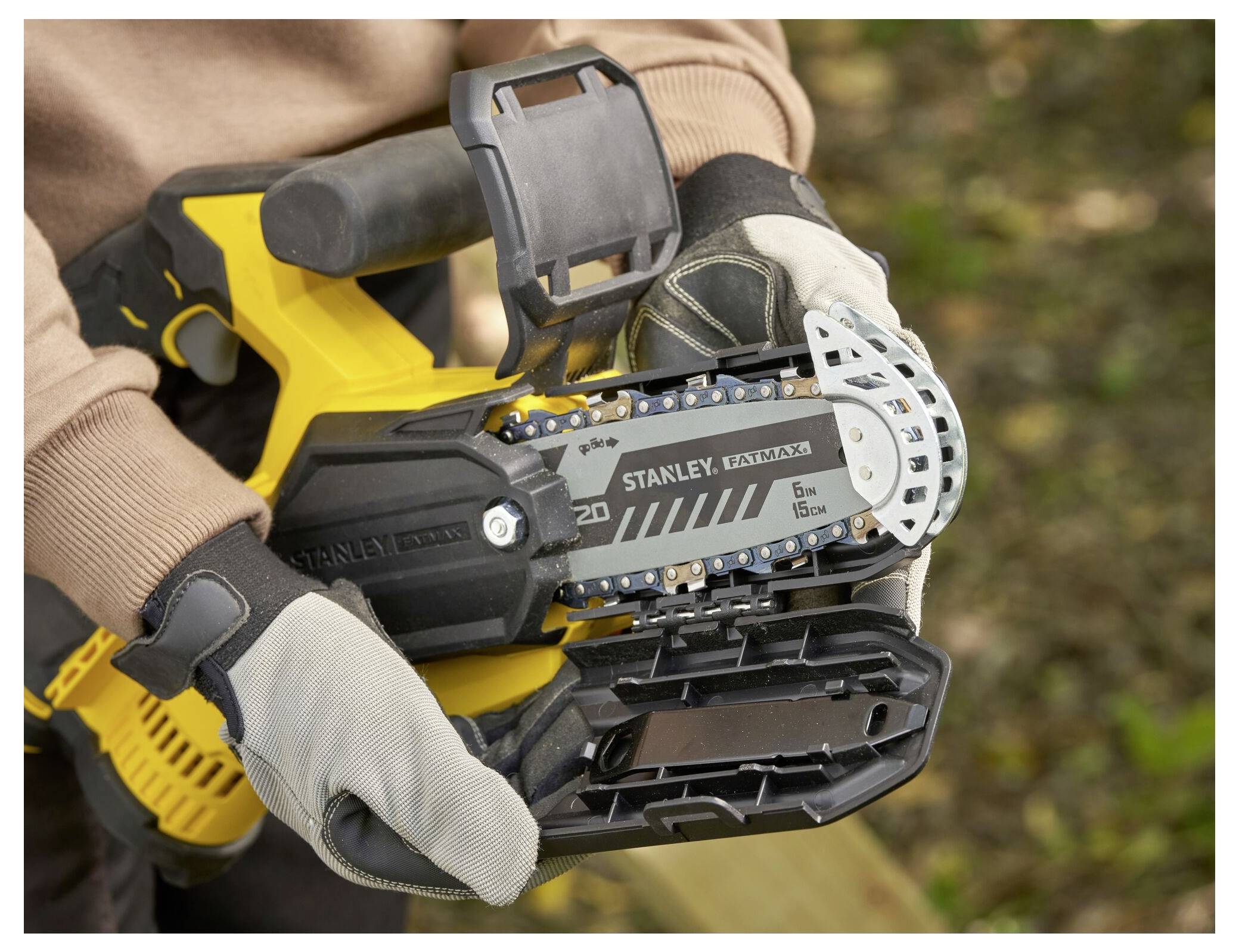 Eine Person hält ein gelbes Elektrowerkzeug mit sichtbarer Kette und Schutzvorrichtung. Das Werkzeug ist eine 'Stanley Fatmax', die zum Schneiden gedacht ist.