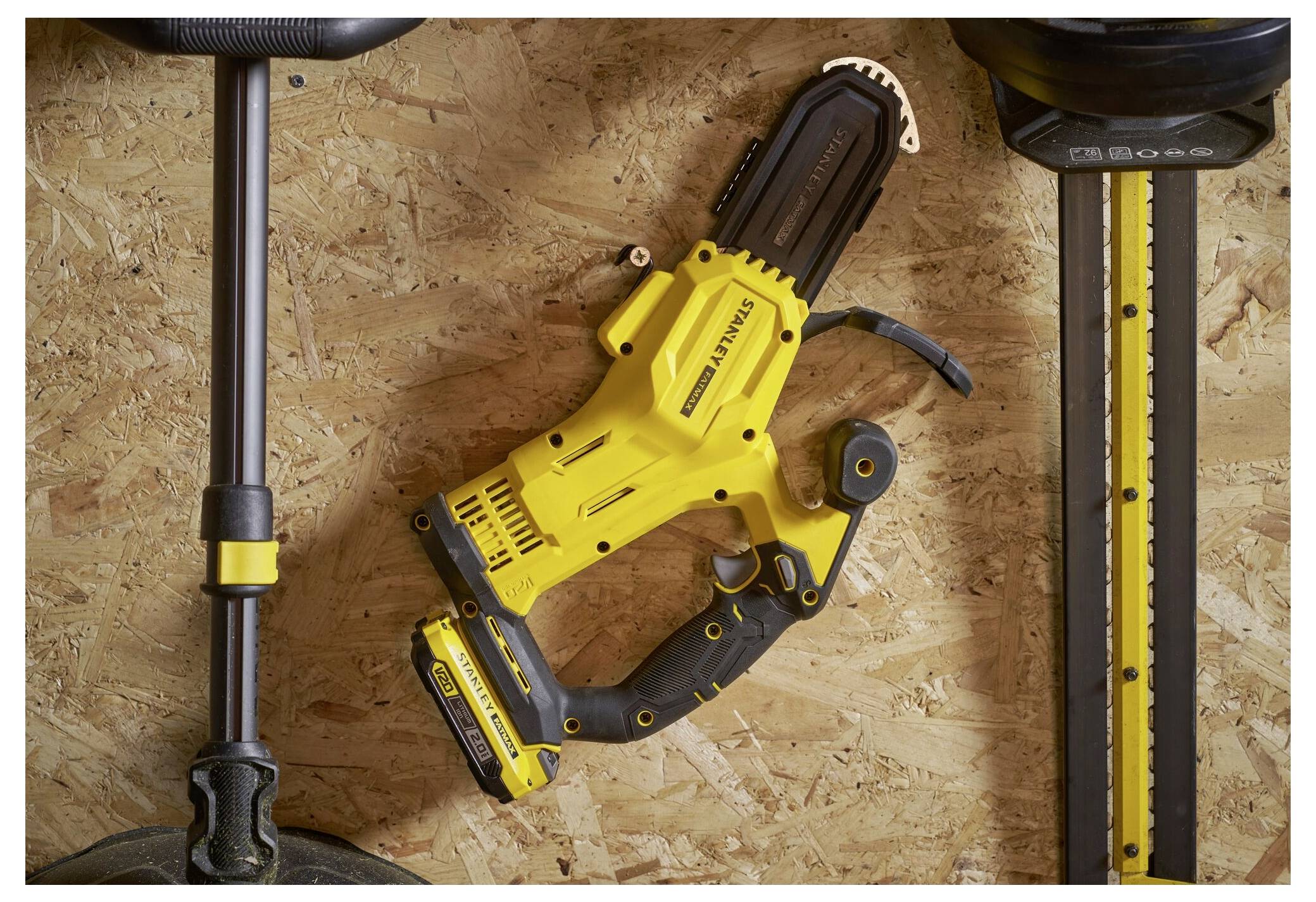 Ein gelbes und schwarzes Elektrowerkzeug ist auf einer Holzoberfläche zwischen zwei langen Werkzeugen platziert, wahrscheinlich als Teil einer Werkstatt- oder Garagenumgebung.
