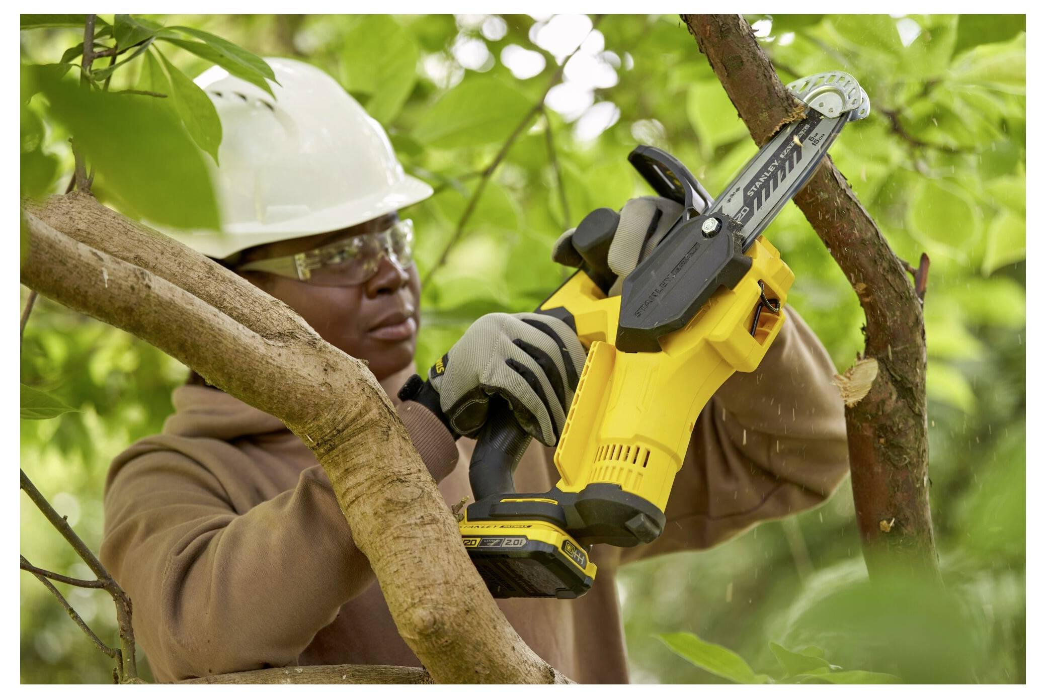 Eine Person in Schutzausrüstung verwendet eine gelbe elektrische Säge, um Äste in einem Waldgebiet zu schneiden.