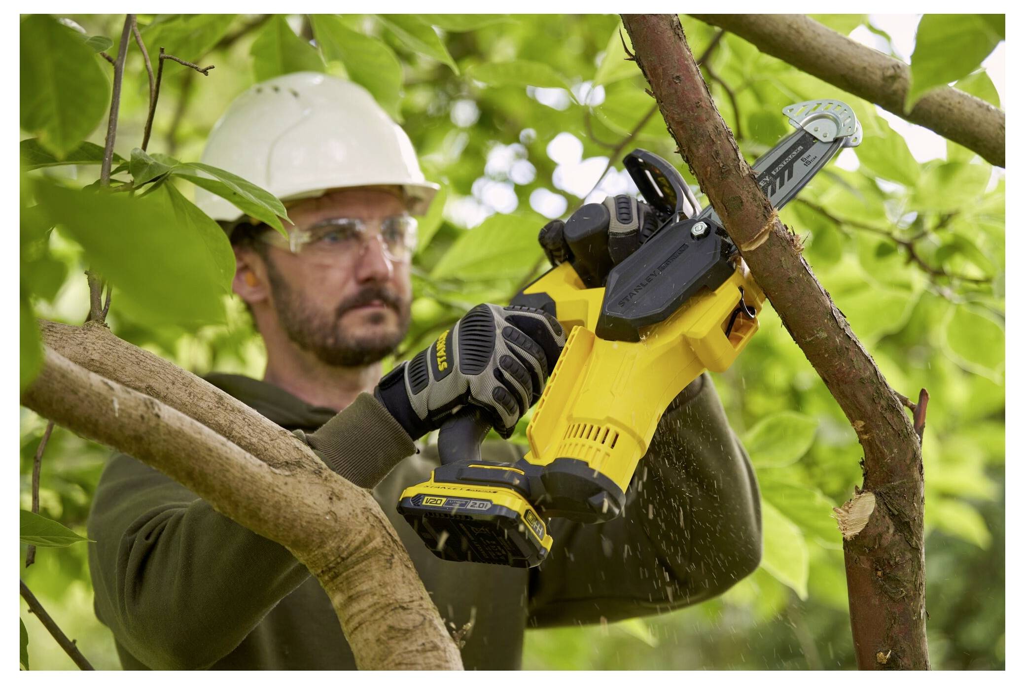 Eine Person in Schutzausrüstung nutzt eine gelbe Elektrokettensäge, um Äste in einer Gartenumgebung zu schneiden.
