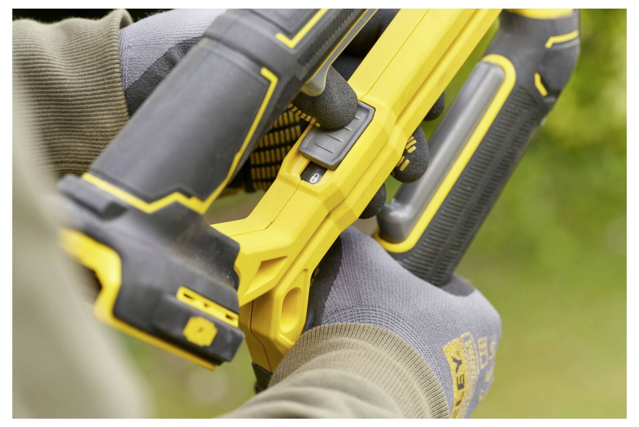 Eine Person, die ein gelbes Elektrowerkzeug mit behandschuhten Händen hält, konzentriert sich auf die Anpassung eines Schalters am Werkzeug, was auf Verwendung oder Wartung hindeutet.