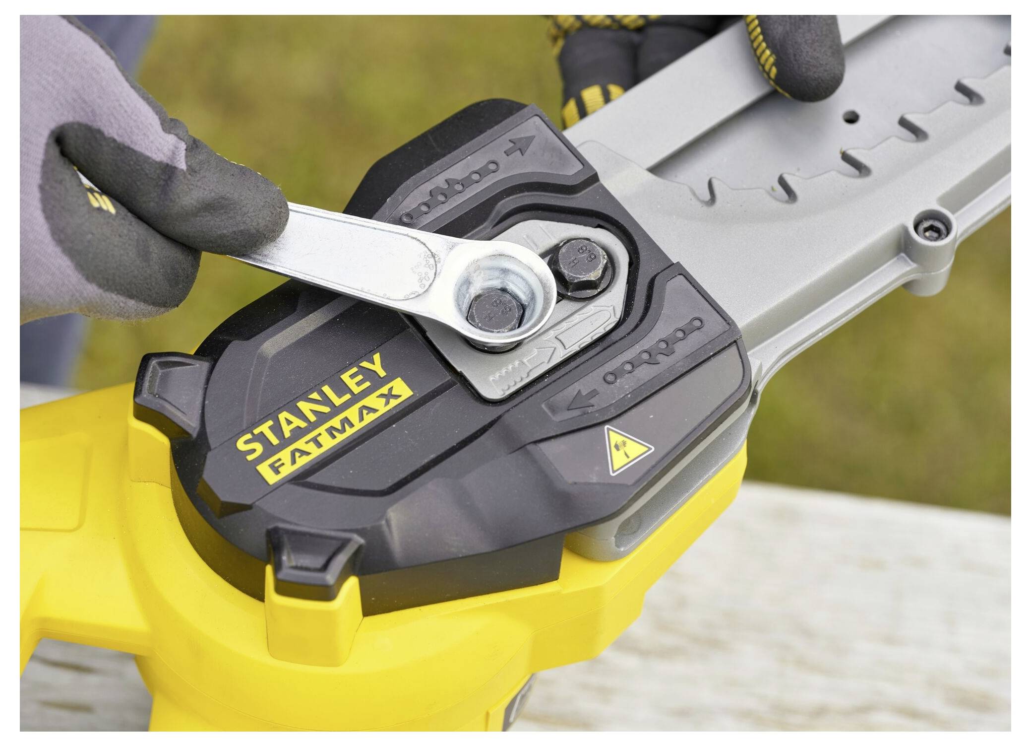 Eine Person mit Handschuhen zieht eine Schraube an einem Kettensägeblatt mit einem Schraubenschlüssel fest. Das Werkzeug ist ein Stanley Fatmax.