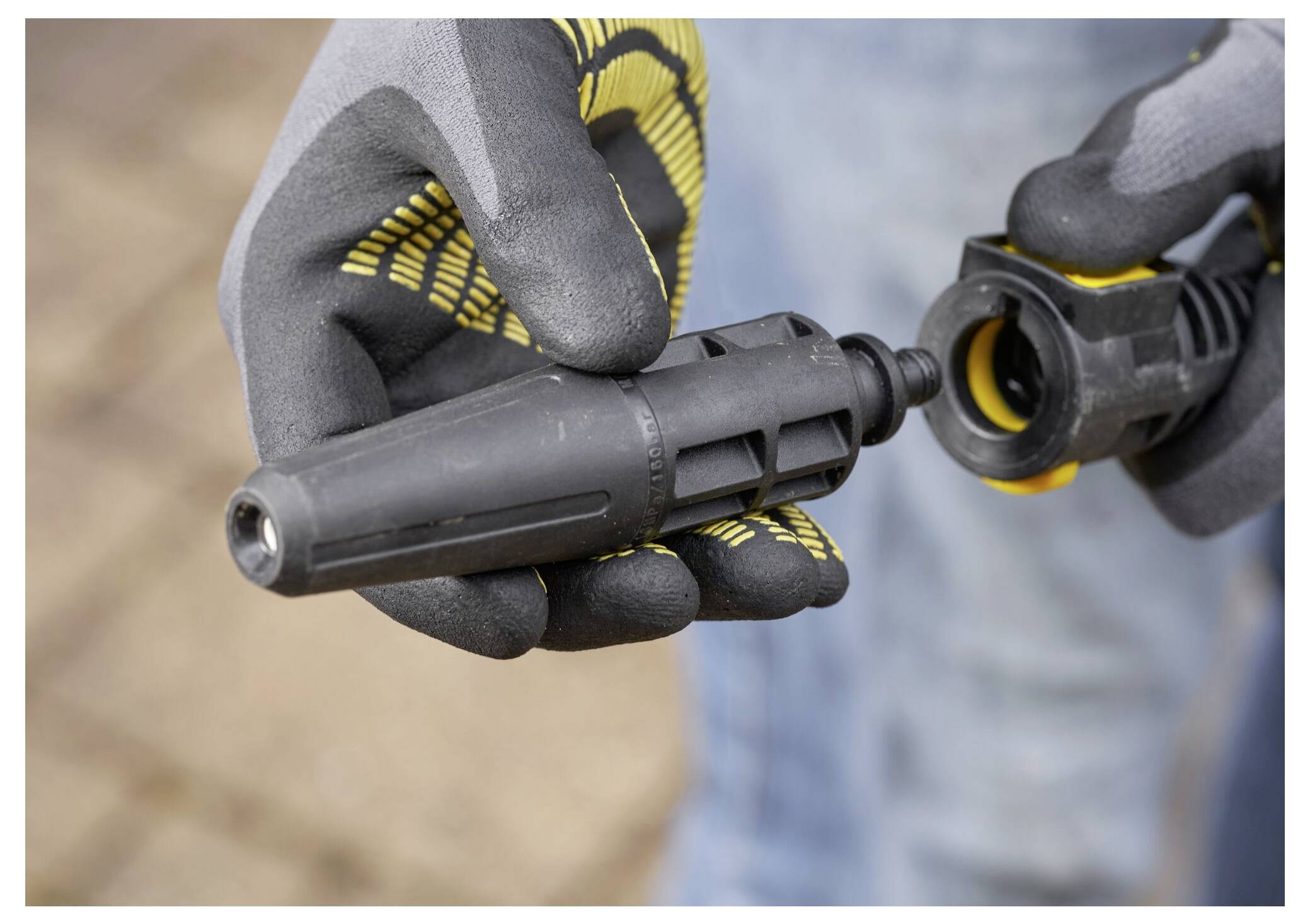 Eine Person, die Handschuhe trägt, befestigt eine Düse an einem Hochdruckreinigungs­schlauch. Die Szene deutet auf Vorbereitungen zum Reinigen oder Waschen hin.