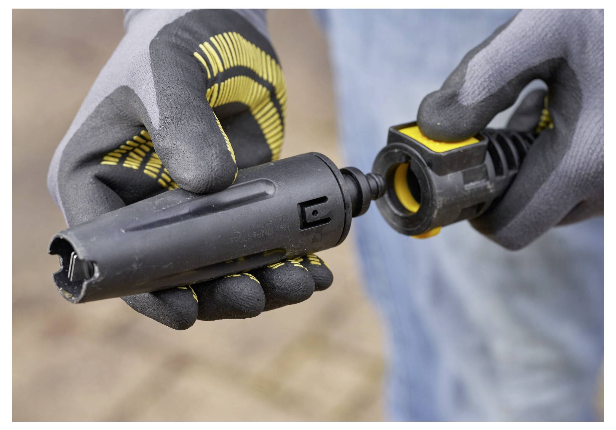 Nahaufnahme von behandschuhten Händen, die zwei Teile einer Hochdruckreiniger-Düse verbinden, was auf eine laufende Montage oder Wartung hindeutet.