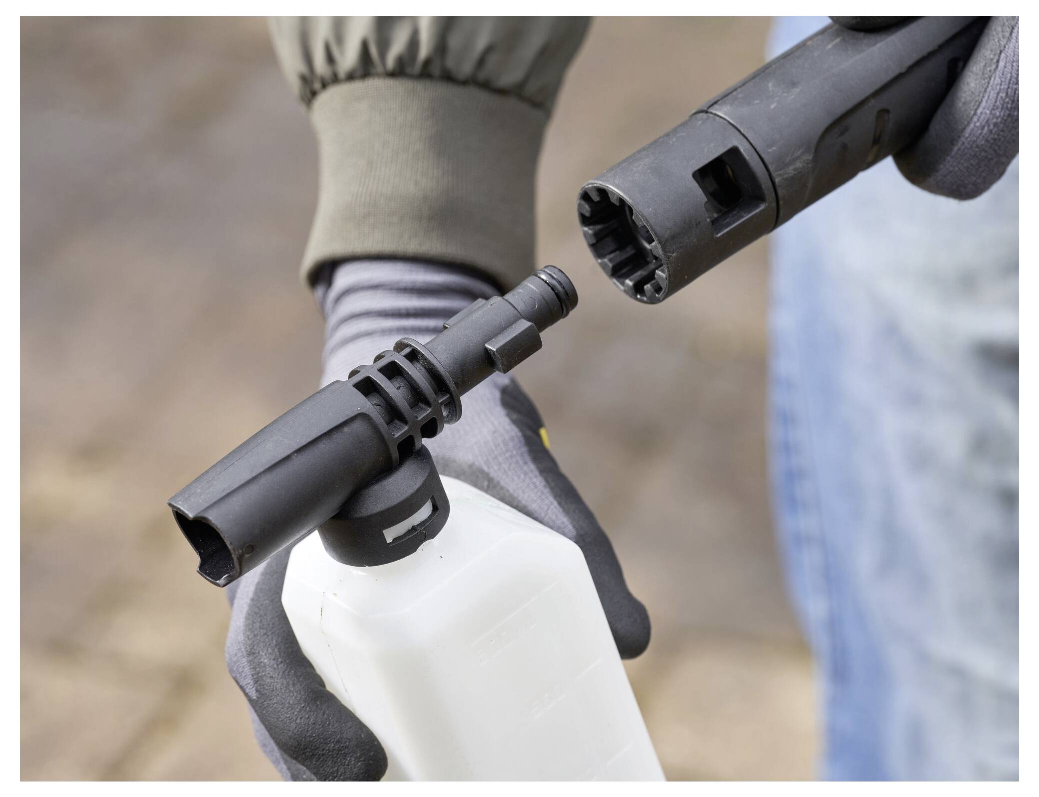 Nahaufnahme von Händen mit Handschuhen, die eine Hochdruckreinigerdüse an eine Sprühflasche anschließen, um sich auf die Reinigung vorzubereiten.