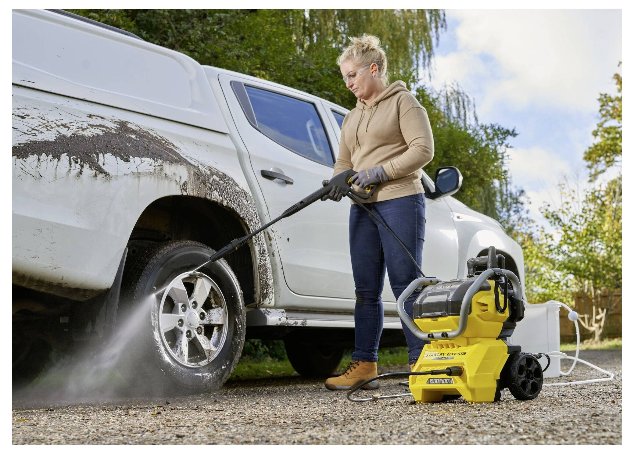 Eine Person nutzt einen Hochdruckreiniger, um Schlamm von einem weißen Pickup-Truck in einer Außenumgebung zu entfernen.