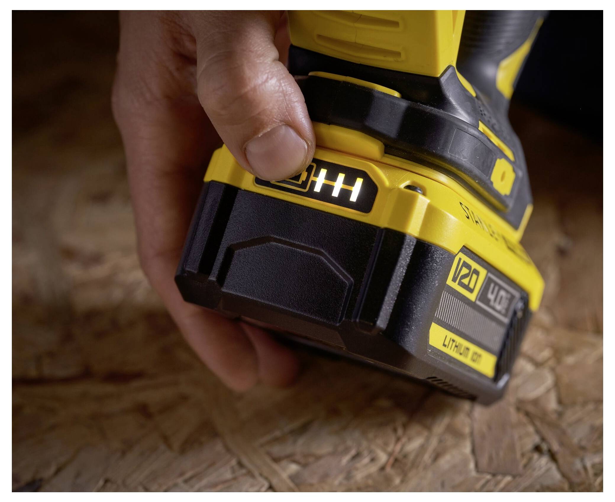 Eine Hand, die ein gelbes Elektrowerkzeug hält, mit Fokus auf den Batteriebereich, zeigt einen Ladeanzeiger mit drei leuchtenden Balken.