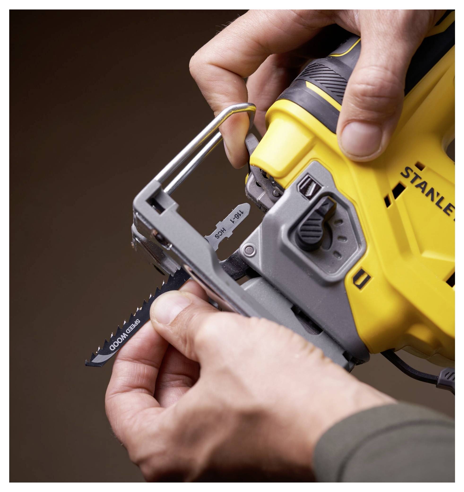 Eine Person bedient eine gelb-graue Stanley-Stichsäge und stellt die Klinge ein. Das Werkzeug wird fest gehalten und betont seine Funktionalität und ergonomisches Design.