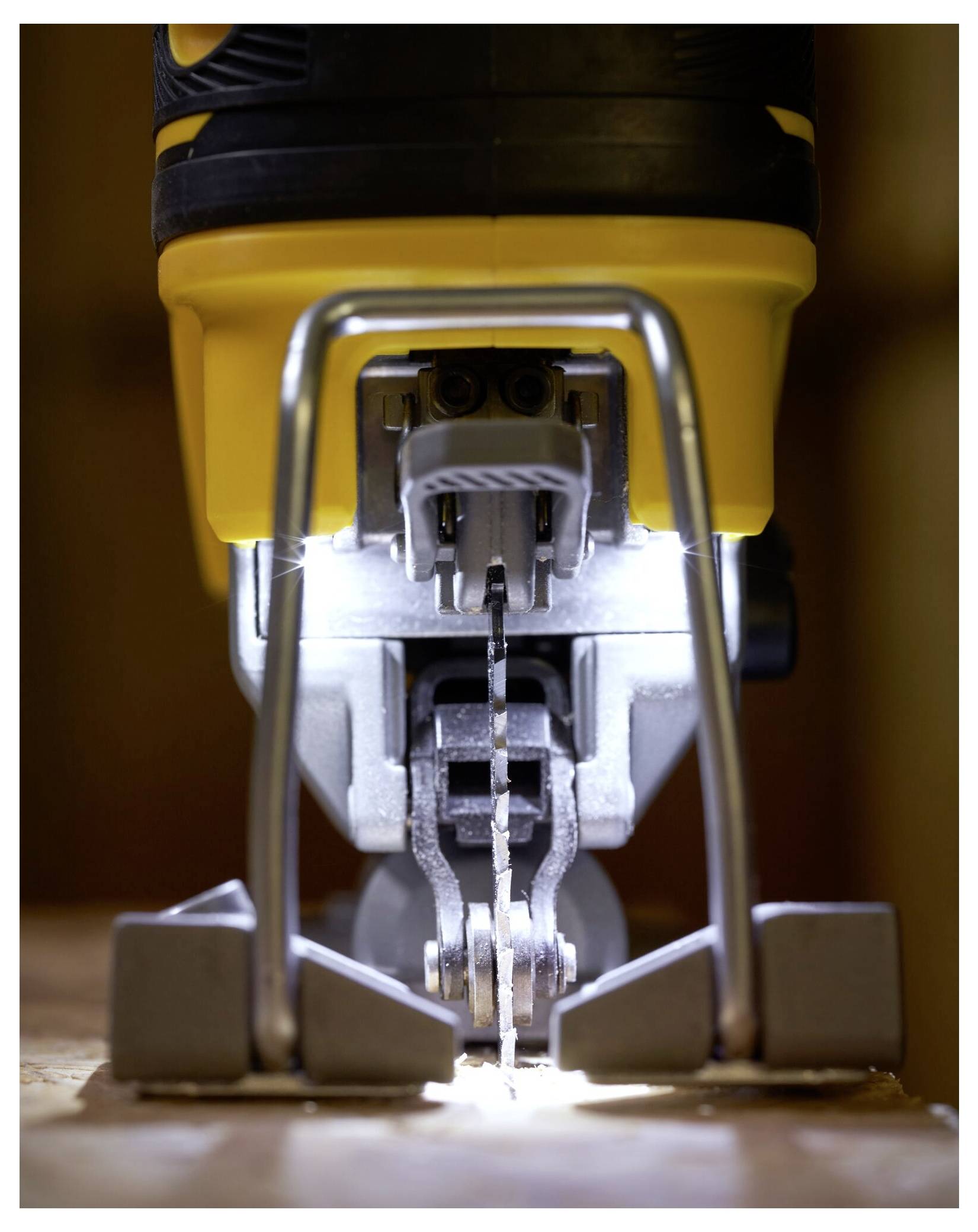 Eine Stichsäge schneidet durch Holz, wobei helles Licht die Klinge und die Umgebung ausleuchtet. Die Maschine ist gelb und silberfarben.