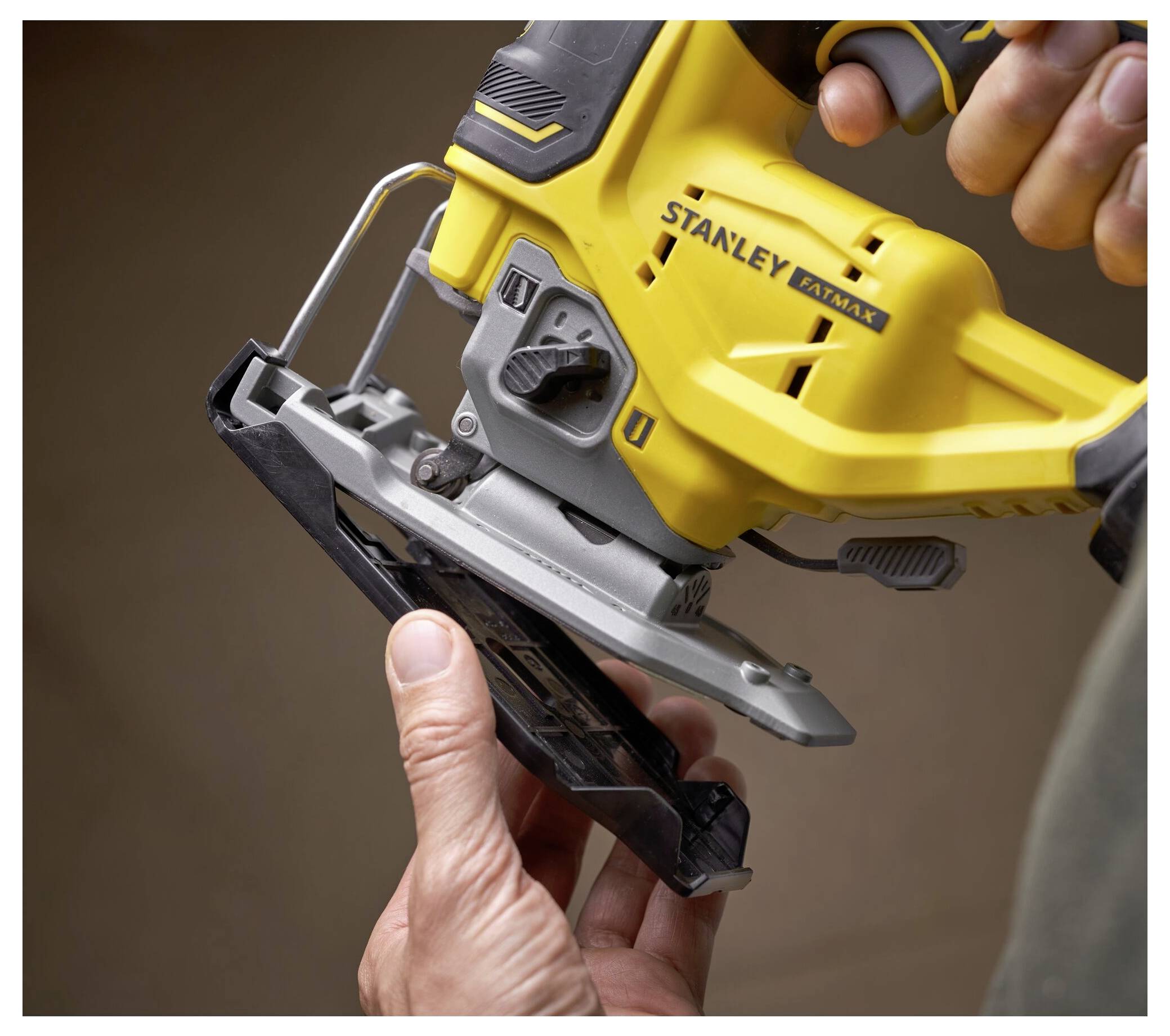 Eine Person stellt ein gelbes Stichsägen-Werkzeug ein, mit Fokus auf das Blatt und den Griff. Die Marke „Stanley