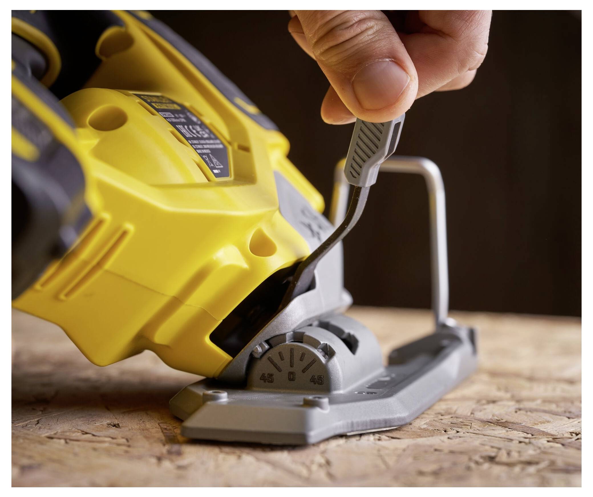 Eine Hand stellt den Winkel an einer gelben elektrischen Stichsäge ein, die auf einer Holzoberfläche positioniert ist, was Werkzeuggebrauch und Anpassung anzeigt.