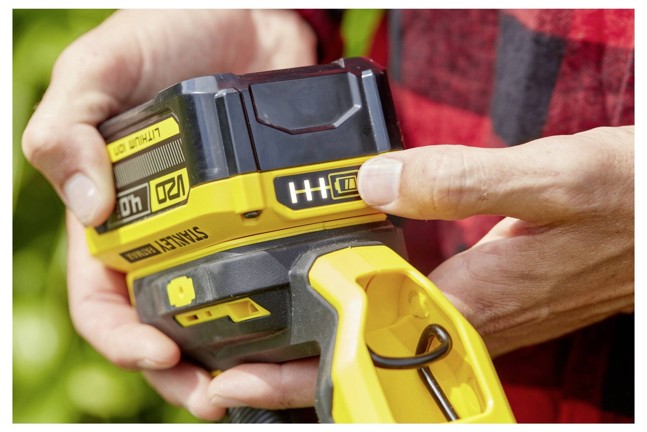 Eine Person hält ein gelb-schwarzes kabelloses Elektrowerkzeug und überprüft die Batteriestandsanzeige, die eine vollständige Ladung anzeigt.
