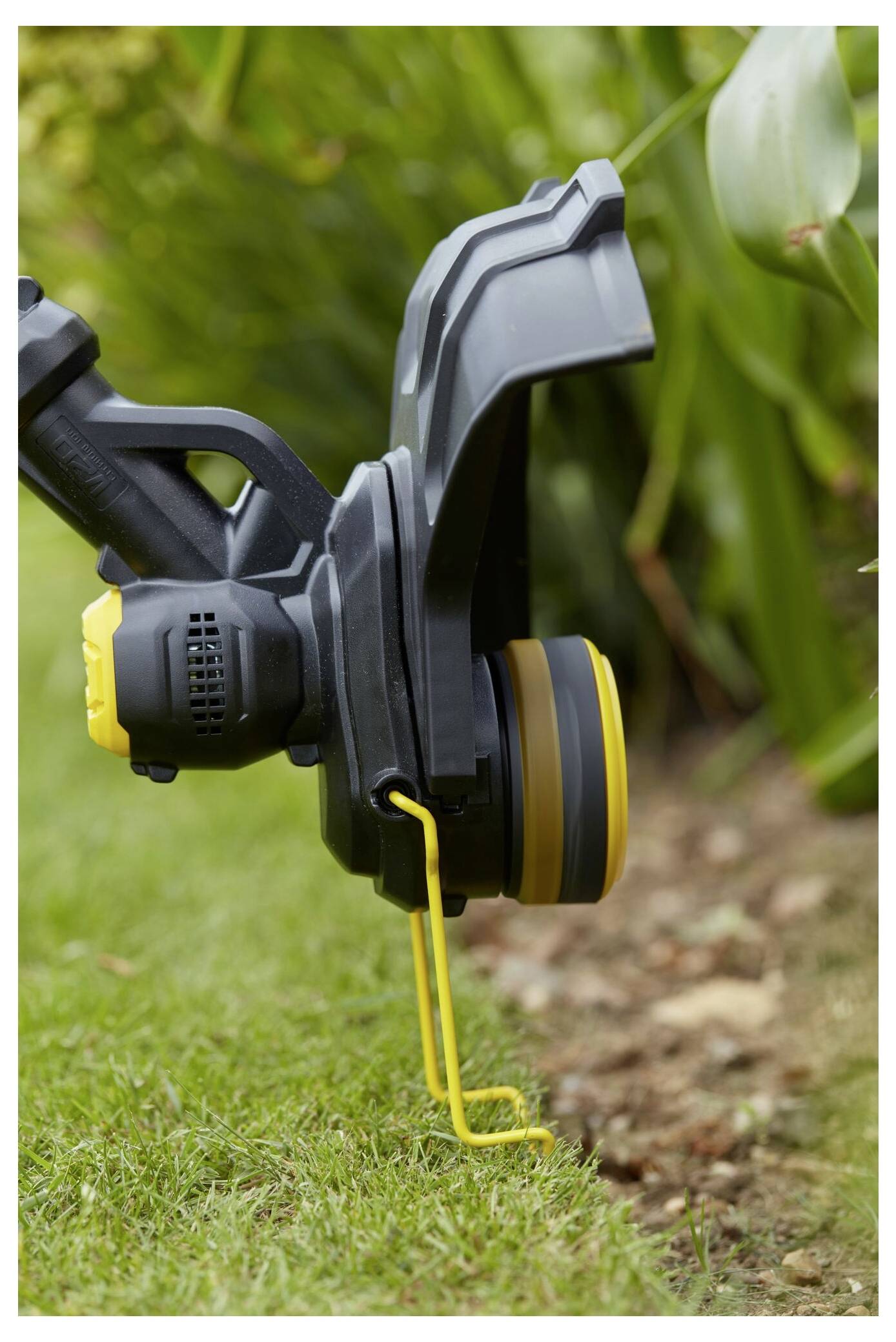 Eine Nahaufnahme eines Rasentrimmers, der entlang eines Beetes verläuft, mit einem schwarz-gelben Schutzbügel, der Gras in der Nähe der Erde schneidet.