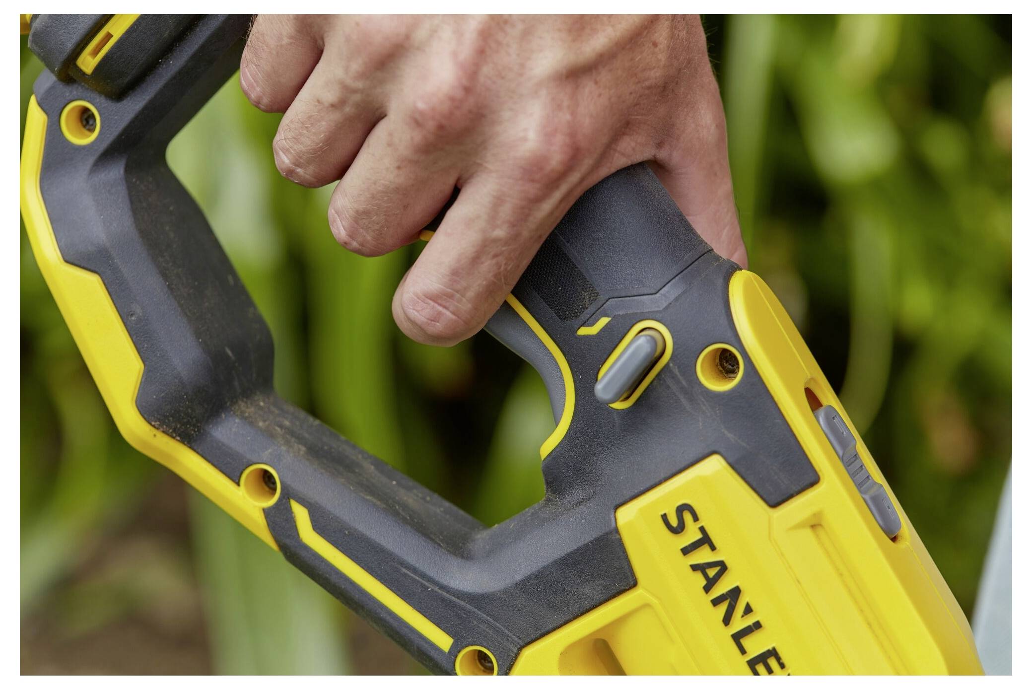 Eine Nahaufnahme einer Hand einer Person, die den Griff eines gelb-schwarzen Elektrowerkzeugs mit der Bezeichnung „STANLEY