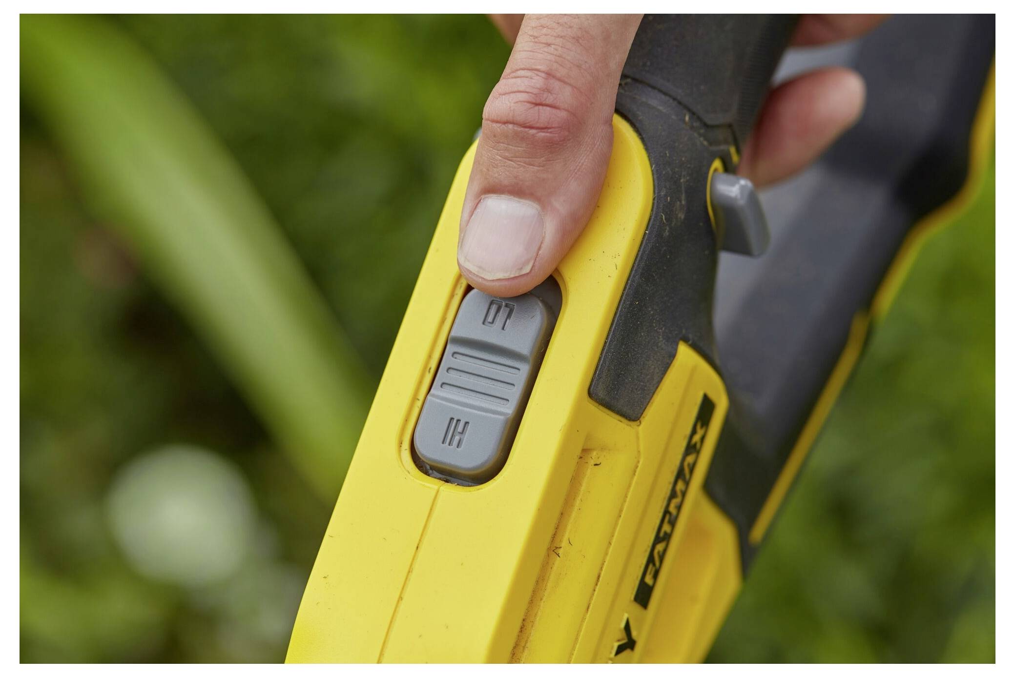 Eine Hand hält ein gelbes elektrisches Gartenwerkzeug mit einer Nahaufnahme des Stromschalters, die die Positionen „EIN