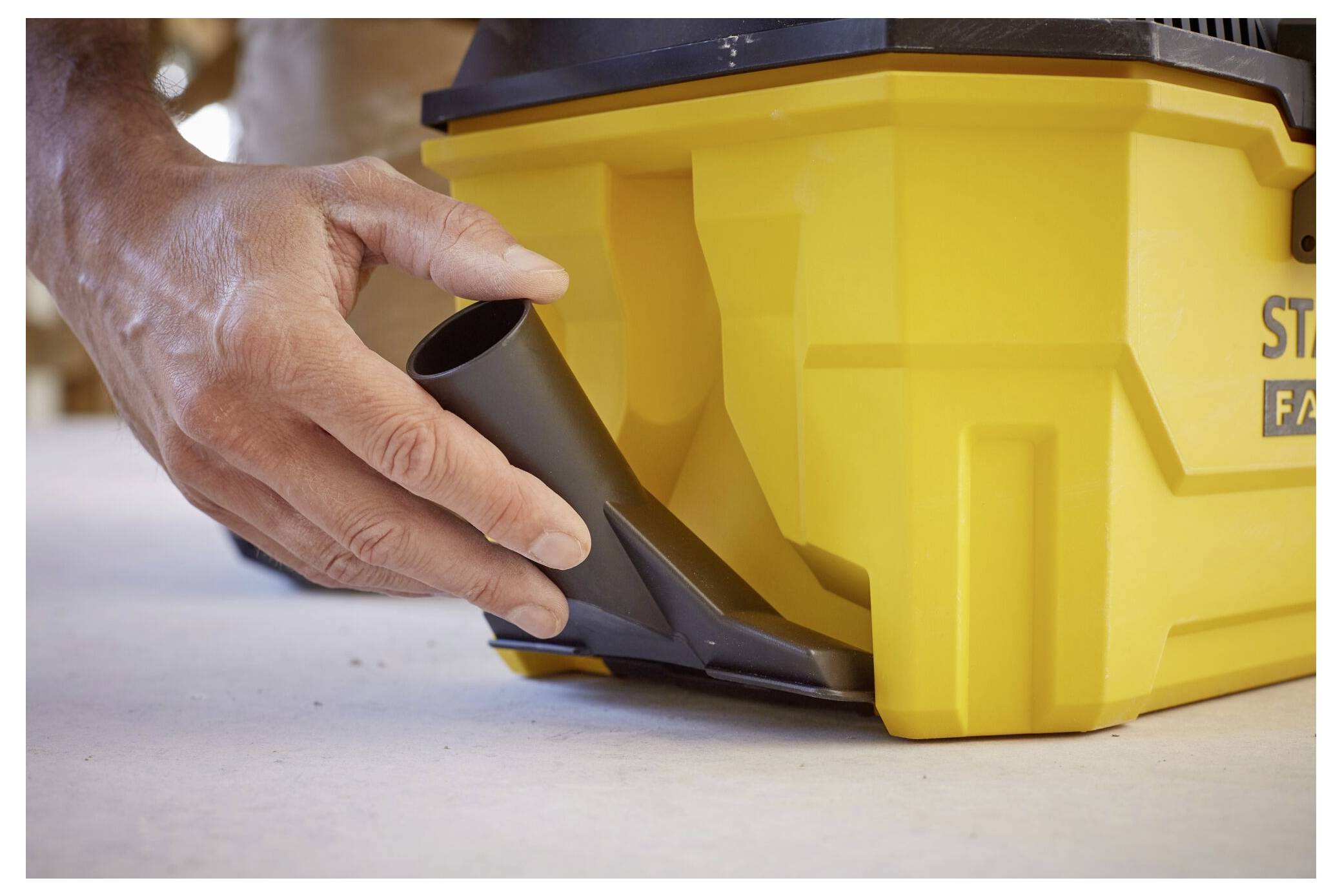 Eine Hand bringt eine breite Düse an einem gelben Industriestaubsauger an, der für Werkstätten oder Baustellen ausgelegt ist und auf die Vorbereitung zur Verwendung hinweist.