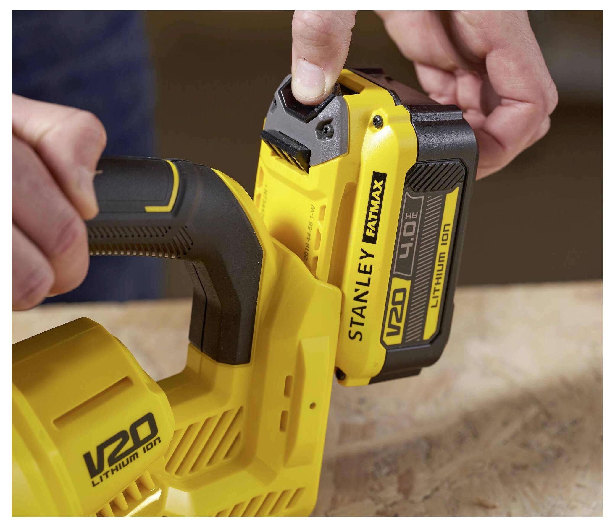 Eine Person setzt einen gelben V20-Lithium-Ionen-Akku in ein Stanley FatMax-Elektrowerkzeug auf einer Holzoberfläche ein.