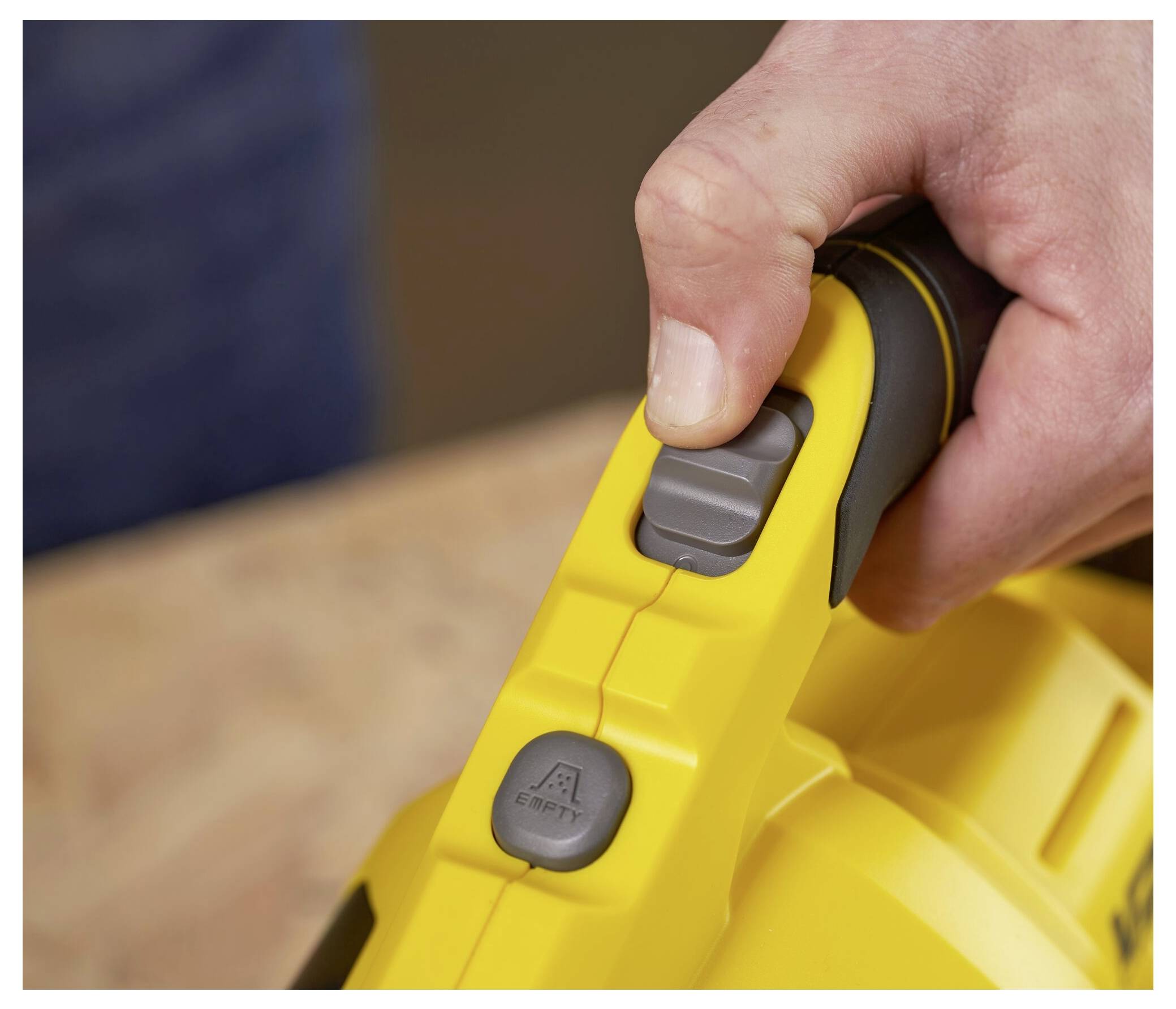 Die Hand einer Person bedient den Netzschalter an einem gelben tragbaren Werkzeug, wobei der Fokus auf dem Daumen liegt, der den grauen Knopf drückt.