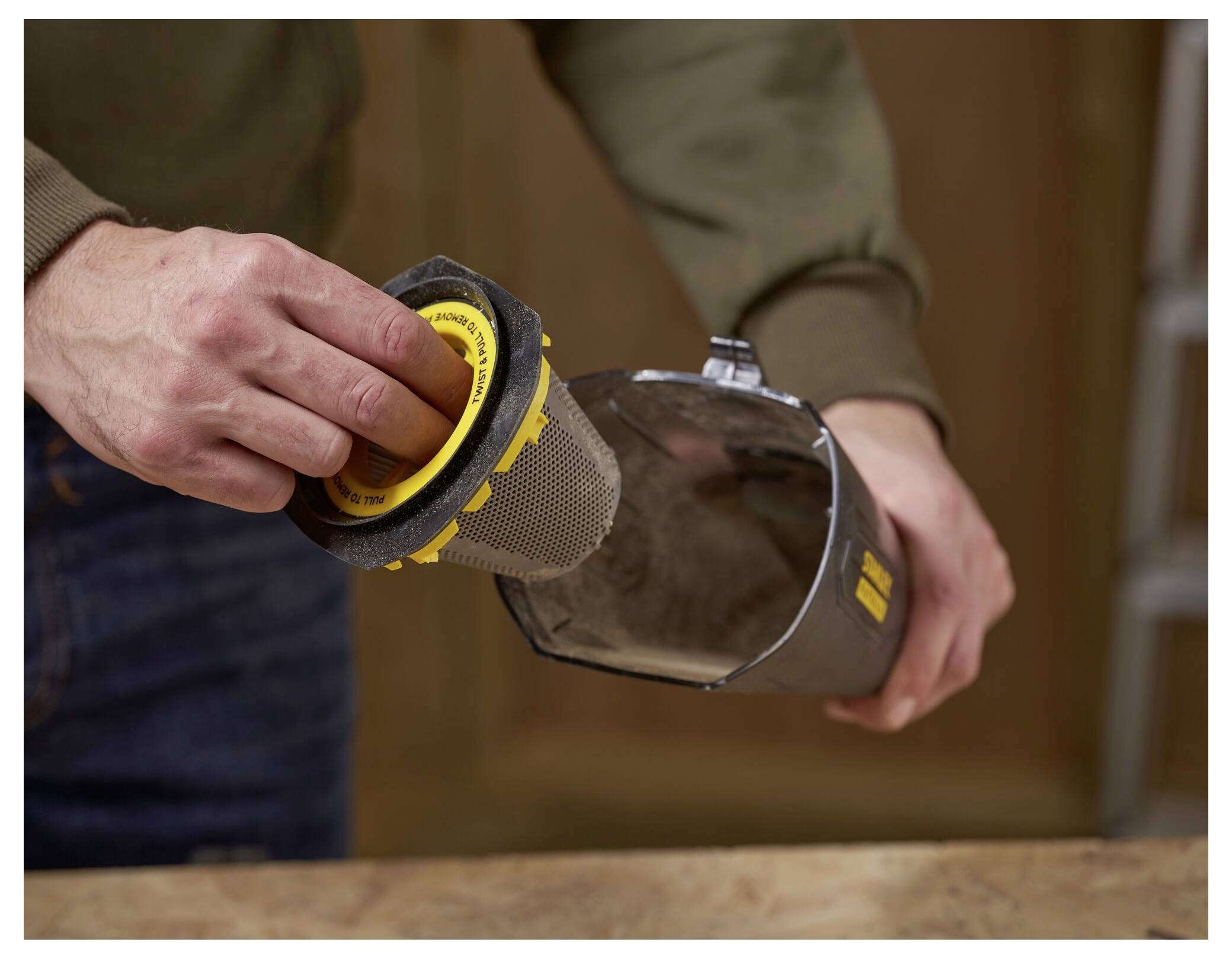 Eine Person leert einen Staubbehälter aus einem kabellosen Staubsauger, während sie den Filter hält, und zeigt damit ein Wartungs- oder Reinigungsverfahren.