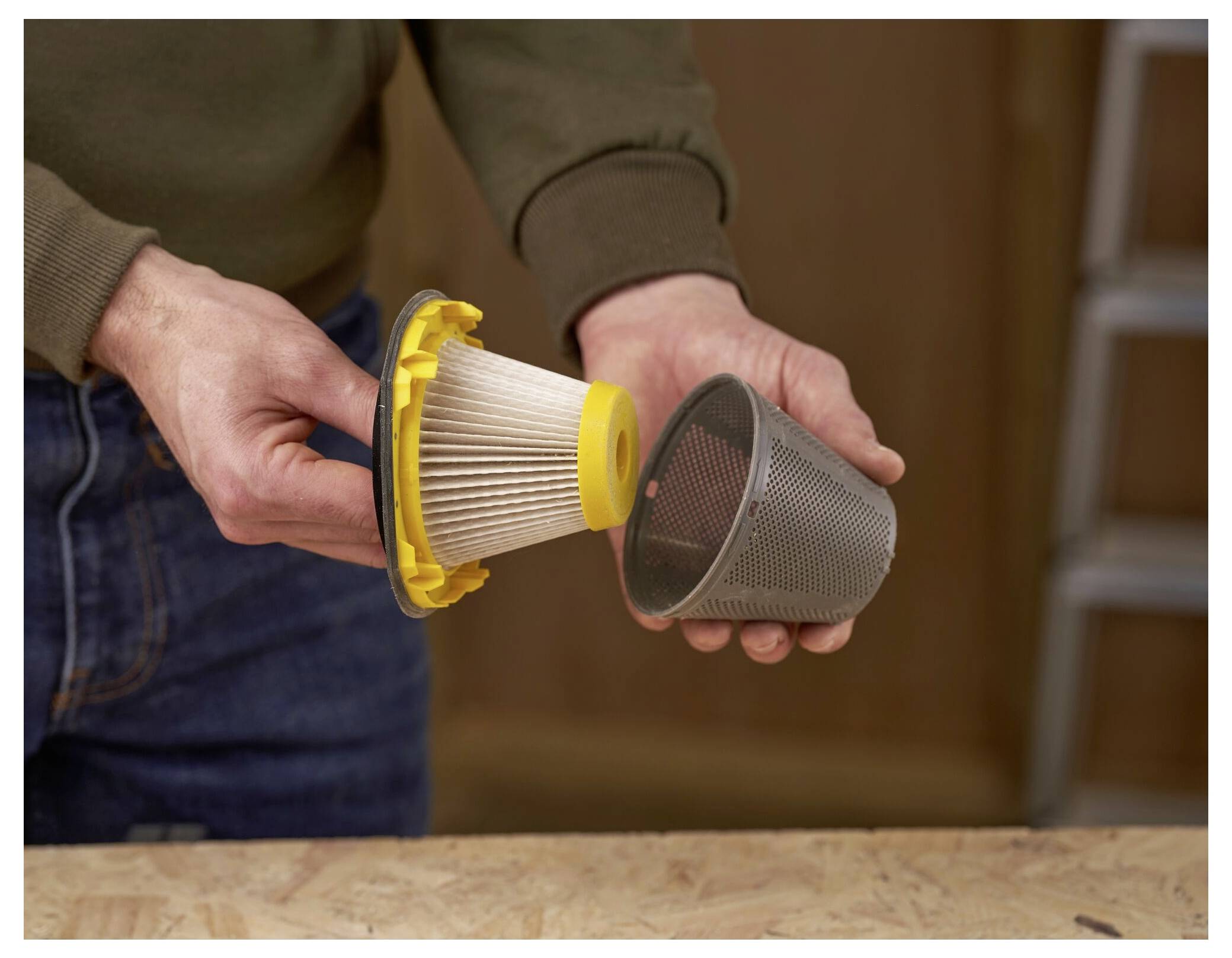 Eine Person demonstriert die Wartung eines Vakuumfilters, indem sie einen Filter mit gelbem Deckel von seinem Schutzgewebe auf einem Holztisch trennt.