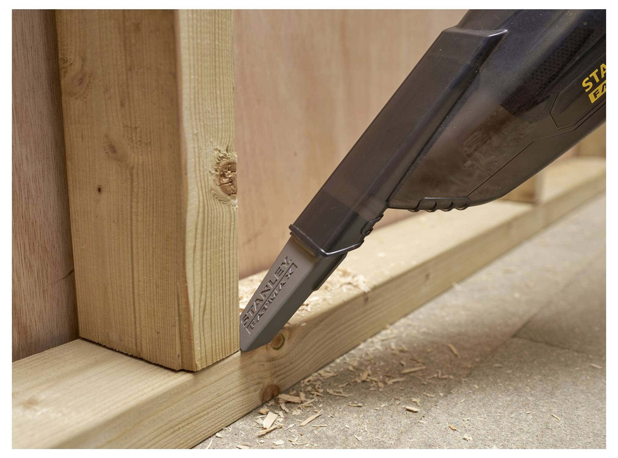 Ein Staubsauger mit einer schmalen Düse reinigt Holzspäne aus der Ecke eines Holzrahmens an einer Wand.