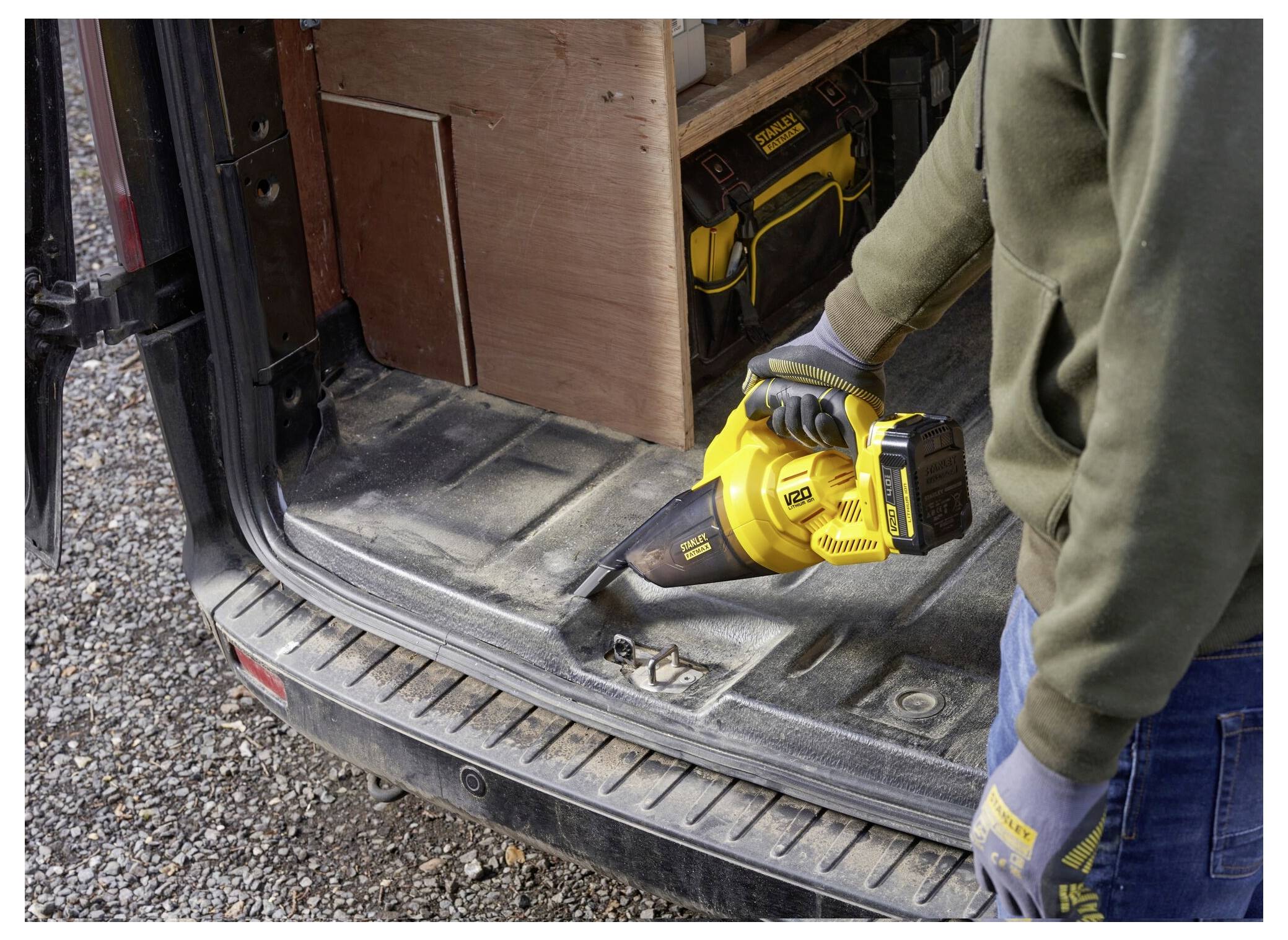 Eine Person benutzt einen gelben Laubblaser, um Schutt von der Rückseite eines Transporters zu entfernen, trägt Schutzhandschuhe und hat Werkzeuge in der Nähe sichtbar.