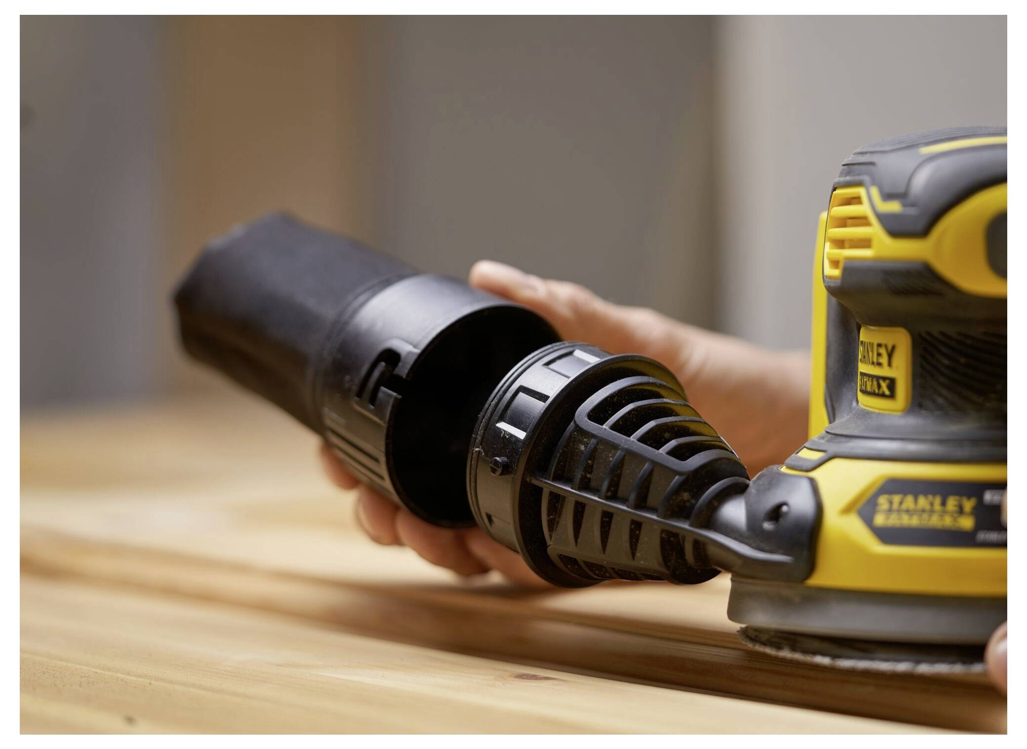 Eine Person montiert einen gelb-schwarzen Elektroschleiffer auf einer Holzoberfläche und konzentriert sich dabei auf die Befestigung des Staubsammelbehälters.