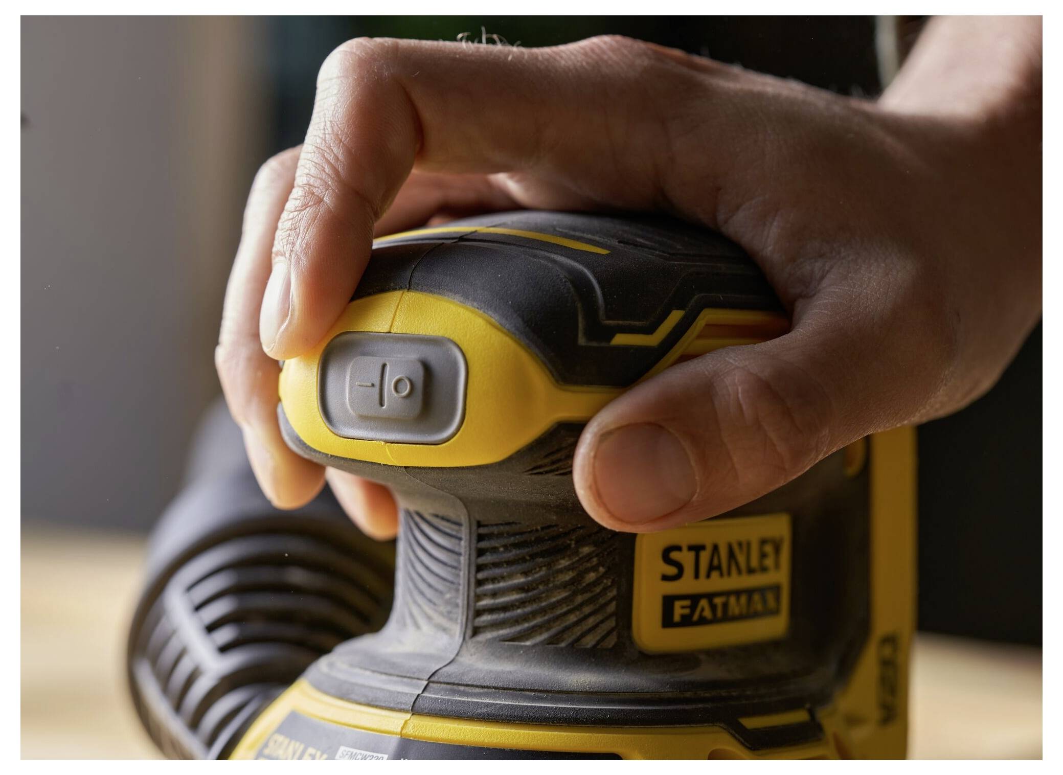 Eine Hand hält ein Stanley Fatmax Elektrowerkzeug, mit einem Finger auf dem Stromschalter, bereit zur Verwendung.