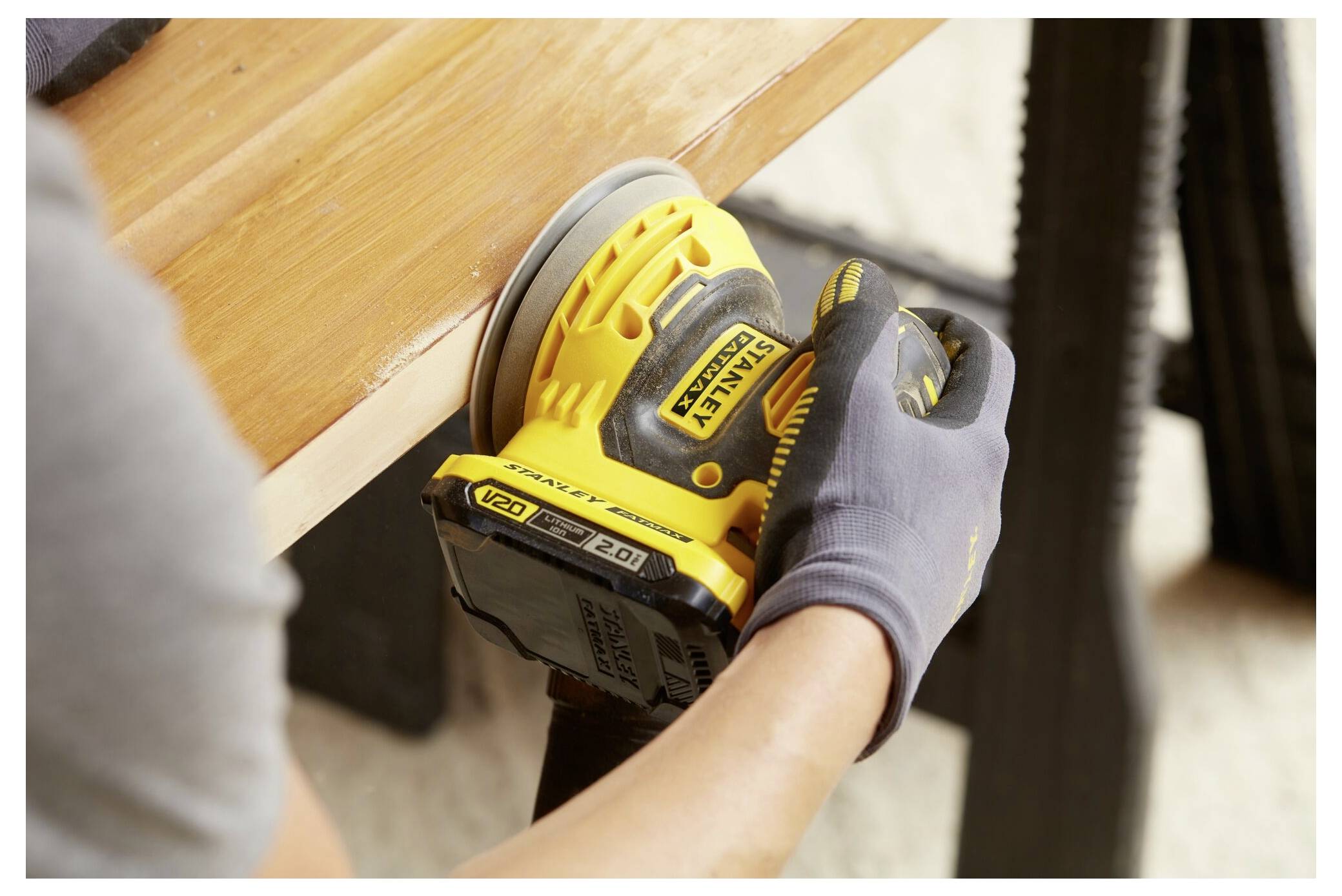 Eine Person, die einen gelben Elektroschleiffer verwendet, um die Kante einer Holzoberfläche zu glätten, mit Fokus auf das Werkzeug und ihre behandschuhte Hand.