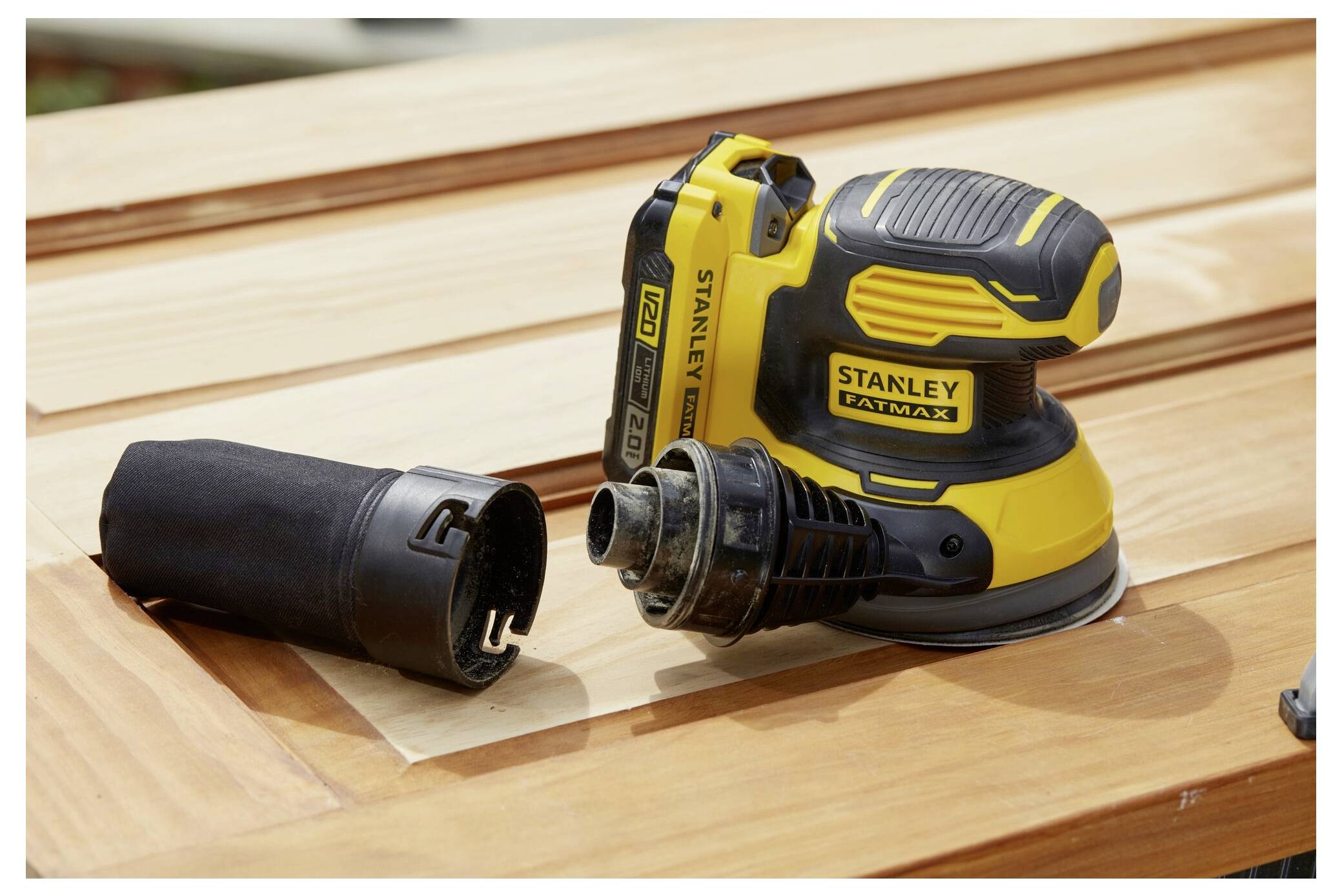 Ein gelb-schwarzer elektrischer Schleiffer ruht auf einer polierten Holzoberfläche, mit einer daneben platzierten Staubsammlervorrichtung.