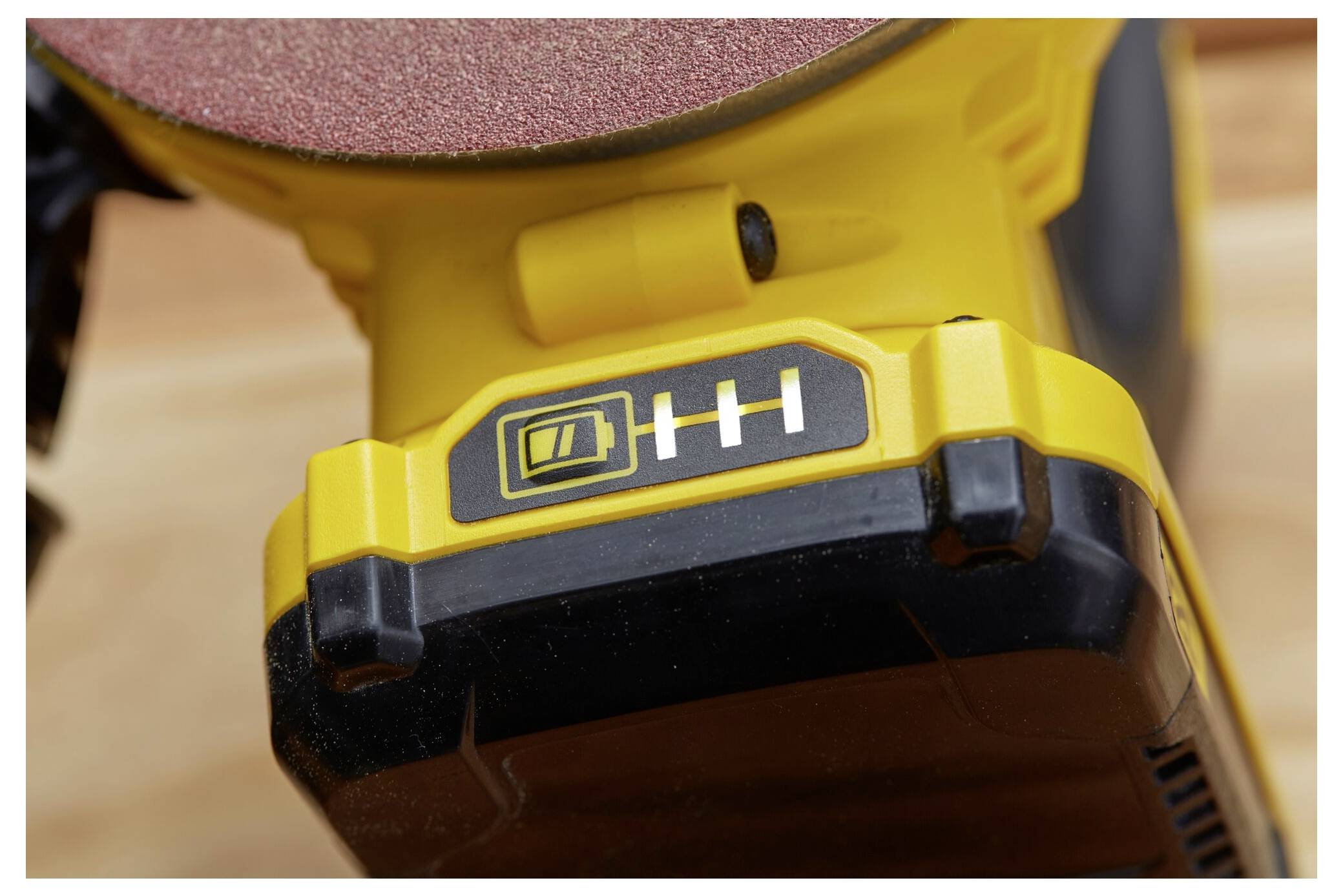 Eine Nahaufnahme einer gelben Akkubatterie für Elektrowerkzeuge mit einem Drei-Balken-Akkuanzeiger, der anzeigt, dass sie vollständig geladen ist.