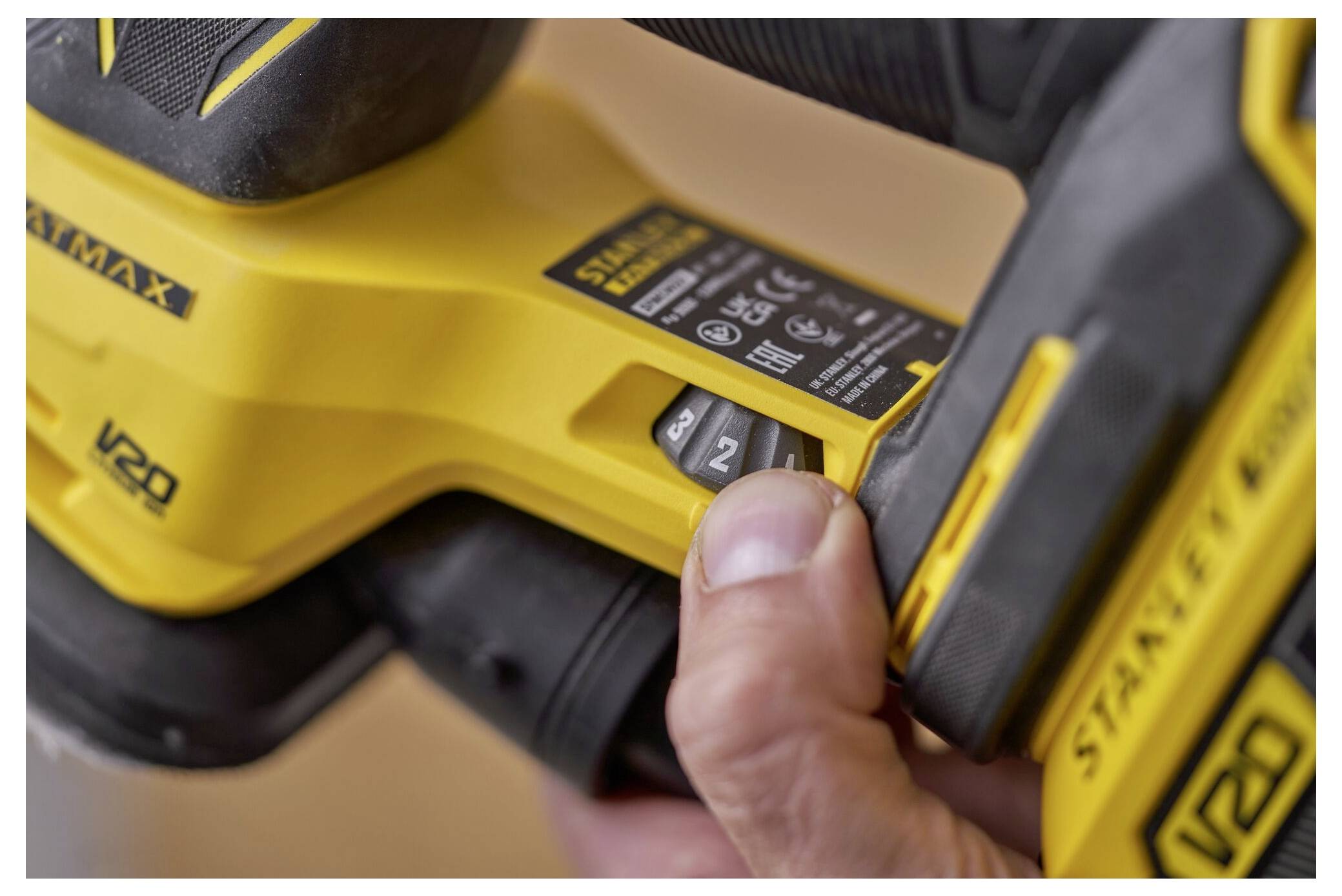 Eine Hand, die ein gelbes Elektrowerkzeug greift, mit zwei sichtbaren Tasten mit den Beschriftungen „1