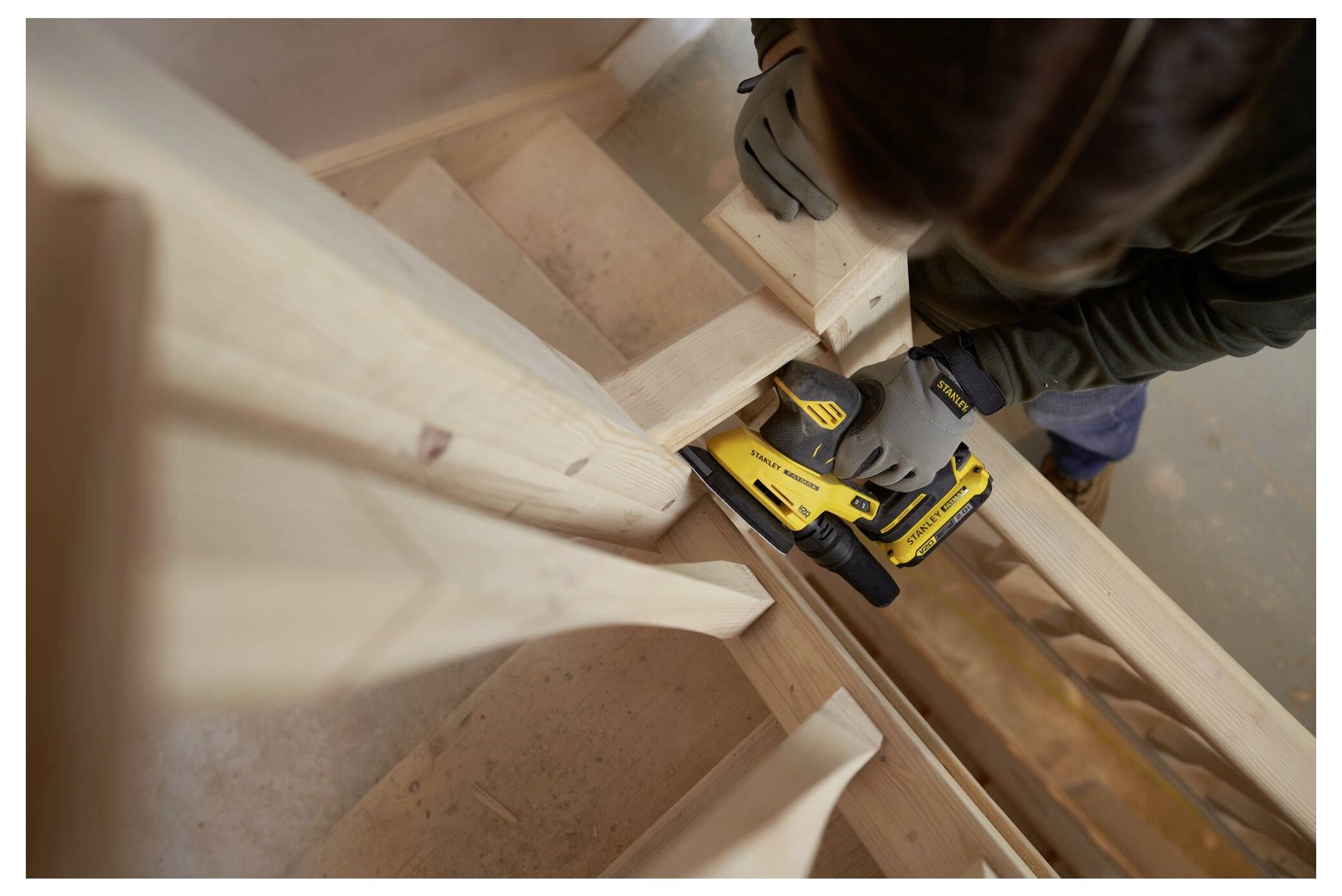 Eine Person verwendet einen gelben Schleifen, um ein Holztreppageländer zu glätten, wobei sie sich auf Präzision und Handwerk konzentriert.