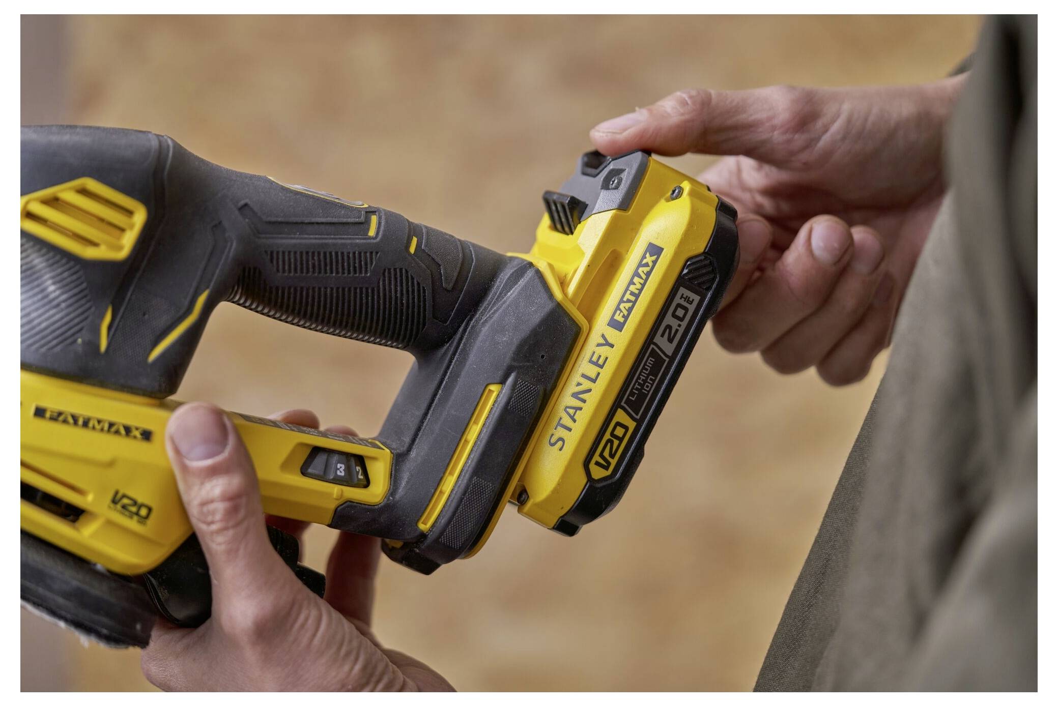 Eine Person setzt eine "Stanley Fatmax V20" 2.0Ah-Batterie in ein Werkzeug ein. Das Werkzeug ist schwarz und gelb mit rutschfestem Griff.