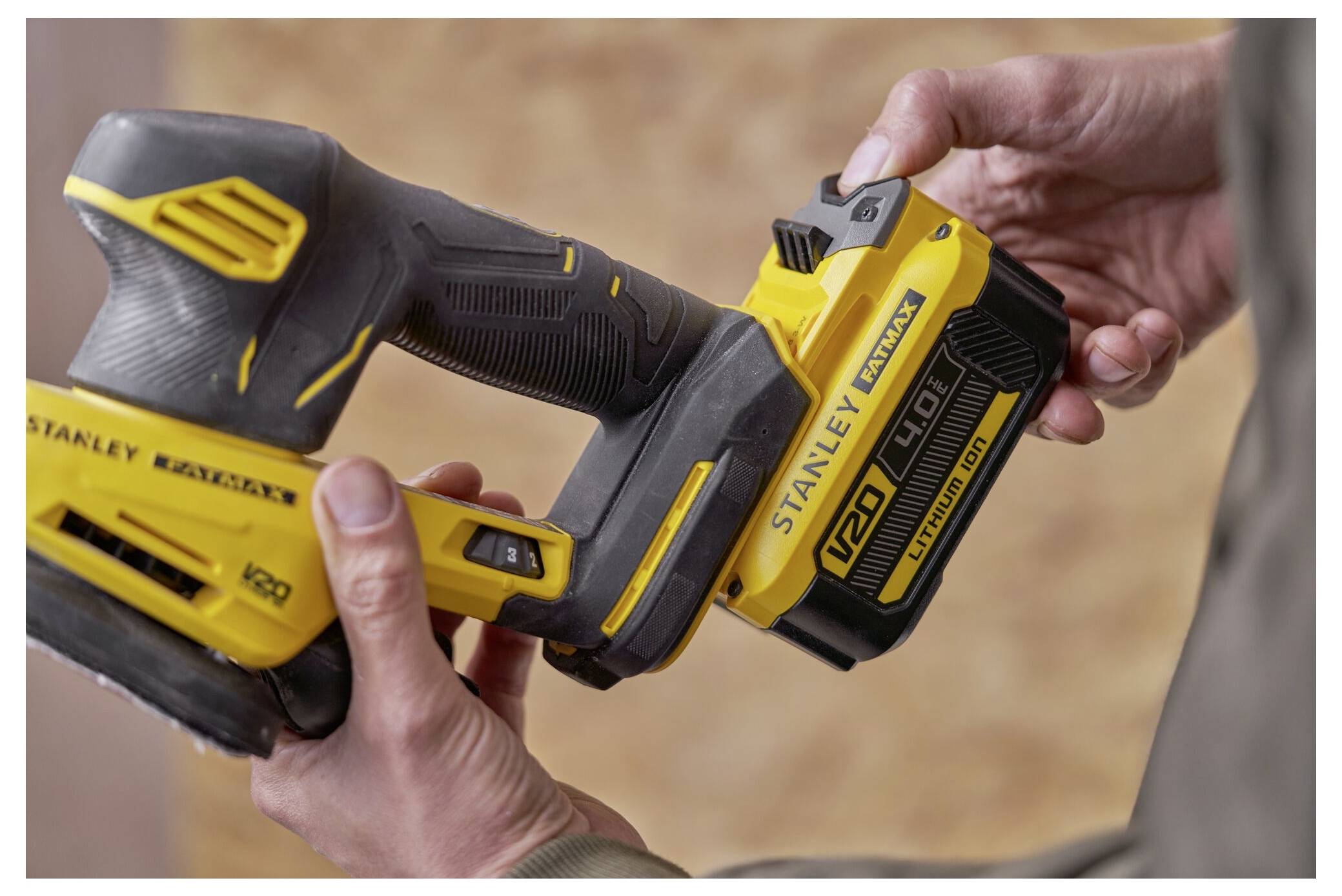 Eine Person, die ein gelbes Elektrowerkzeug mit der Markenbezeichnung "Stanley FatMax V20" hält, wobei der Fokus auf dem Batterieanbaubereich liegt.