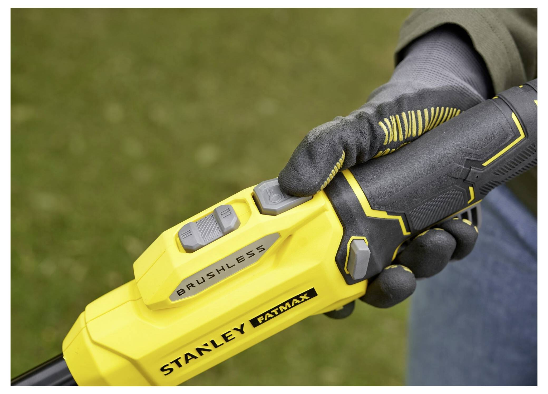 Eine behandschuhte Hand hält ein Stanley Fatmax bürstenloses Werkzeug mit gelben und schwarzen Details, vor einem unscharfen grünen Außenhintergrund.
