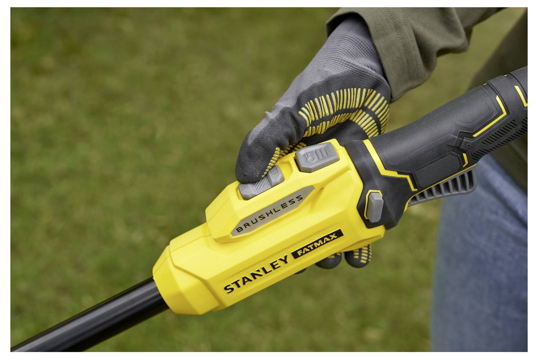 Eine Person hält ein gelb-schwarzes kabelloses Stanley Fatmax Werkzeug. Die Hand ist handschuhiert und der Hintergrund zeigt Gras.