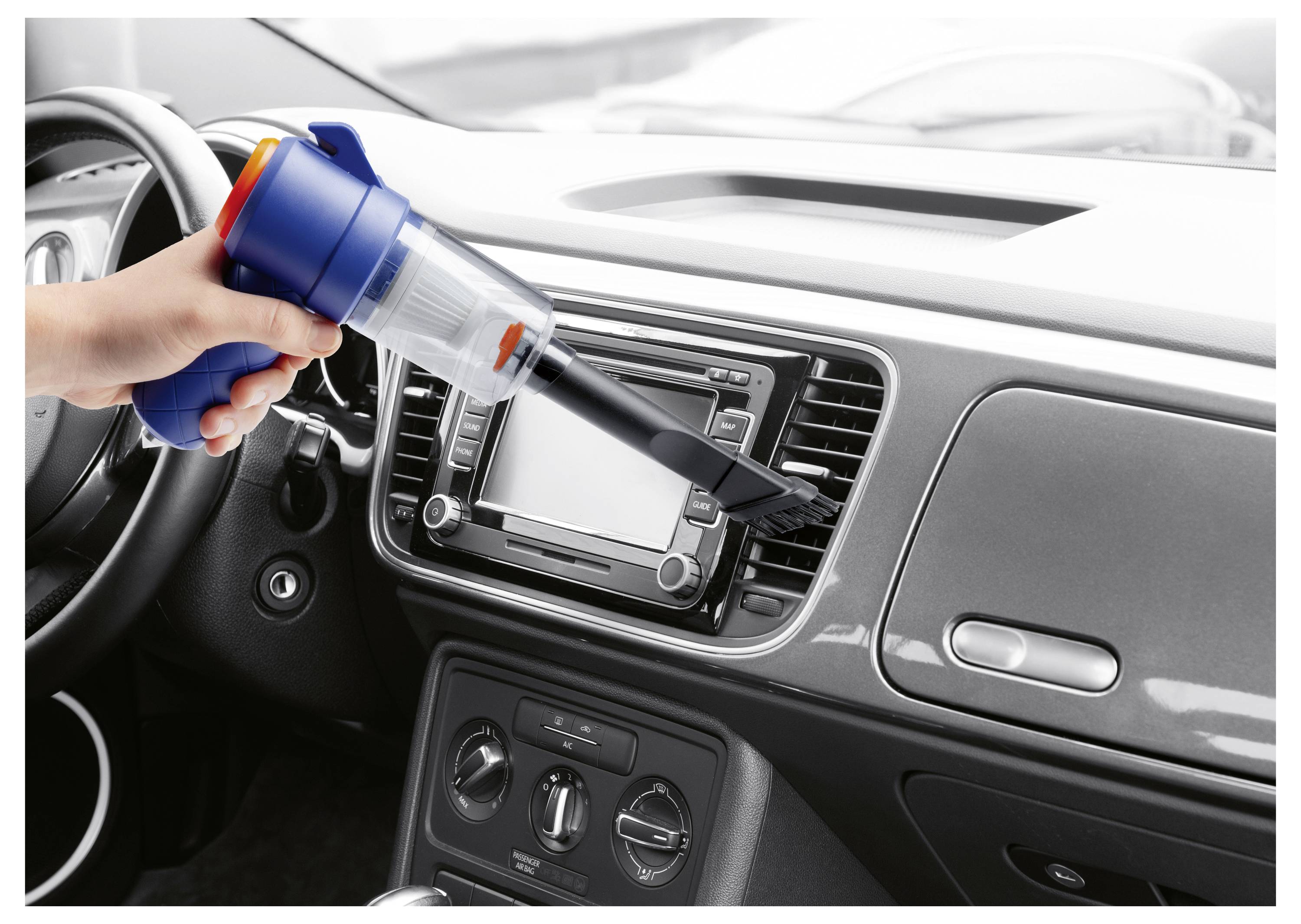 Eine Person, die das Armaturenbrett eines Autos mit einem tragbaren Staubsauger reinigt und sich auf den Lüftungsschlitz auf der Fahrerseite konzentriert.