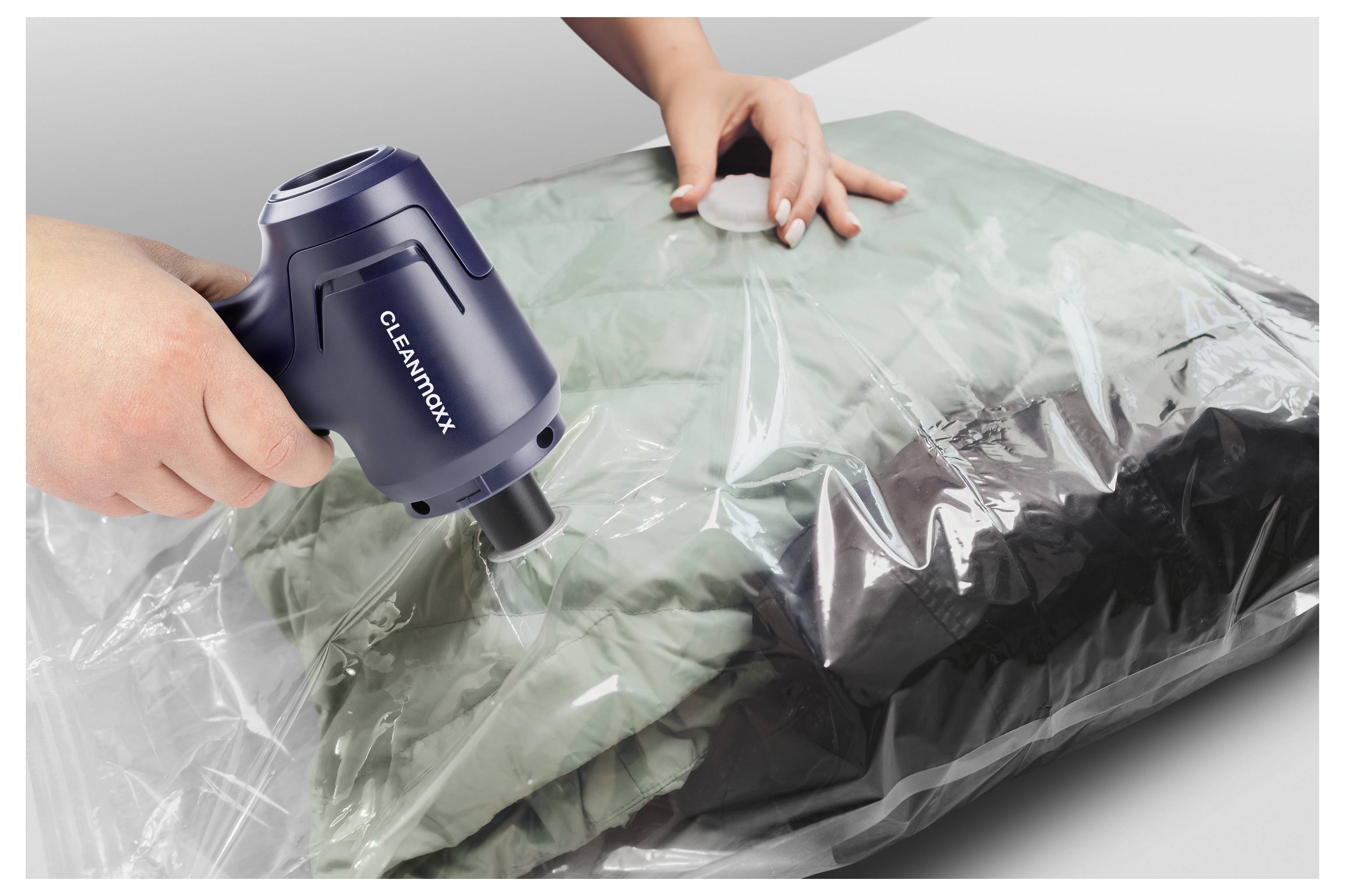 Eine Person benutzt einen CLEANMAXX-Staubsauger, um Luft aus einem versiegelten Lagerbeutel mit Kleidung zu entfernen, um diese für platzsparende Lagerung zu komprimieren.