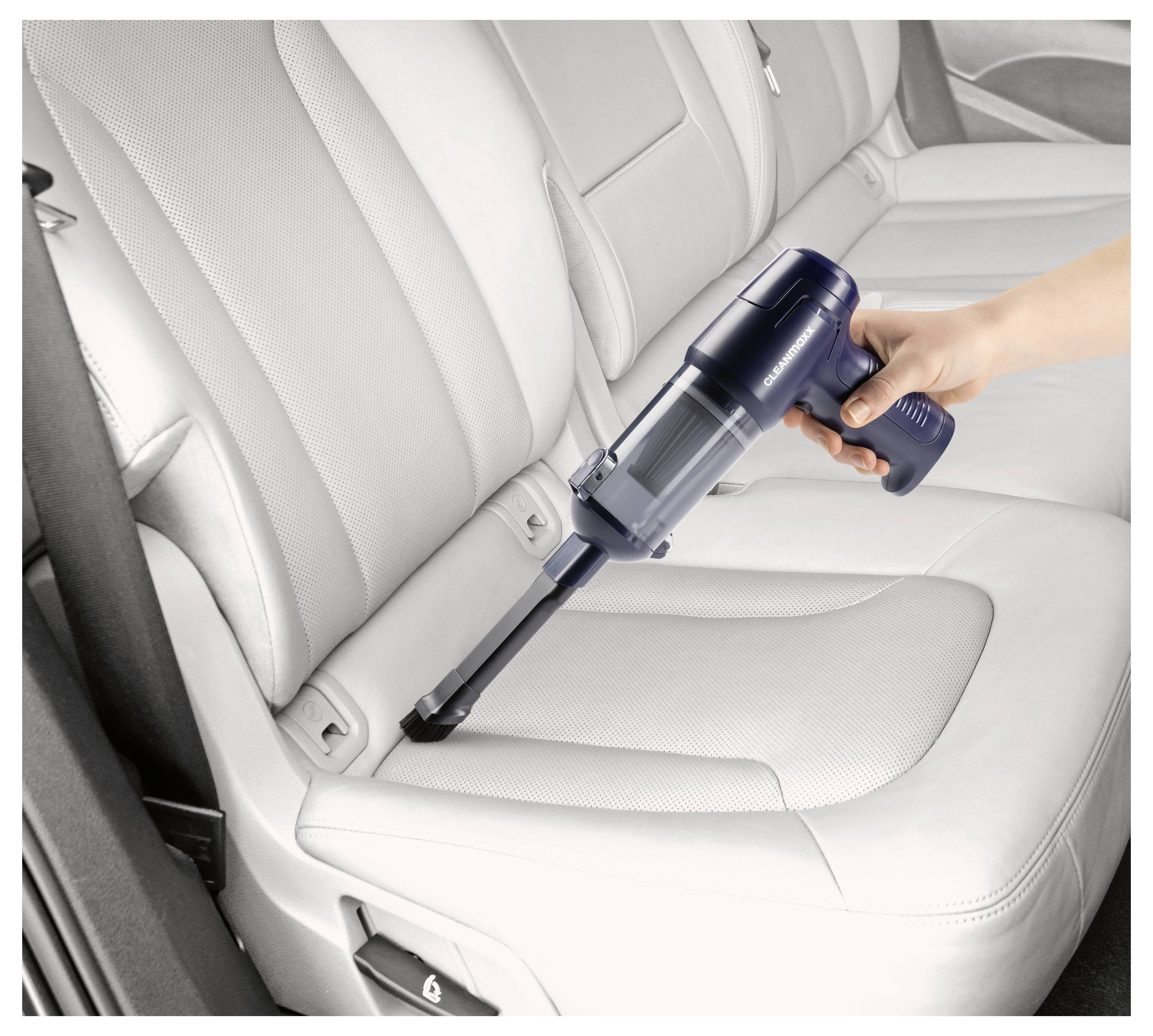 Eine Hand benutzt einen tragbaren Staubsauger, um Verschmutzungen aus den Rillen von hellgrauen Ledersitzen eines Autos zu entfernen und zeigt damit seine Reinigungsfähigkeit.
