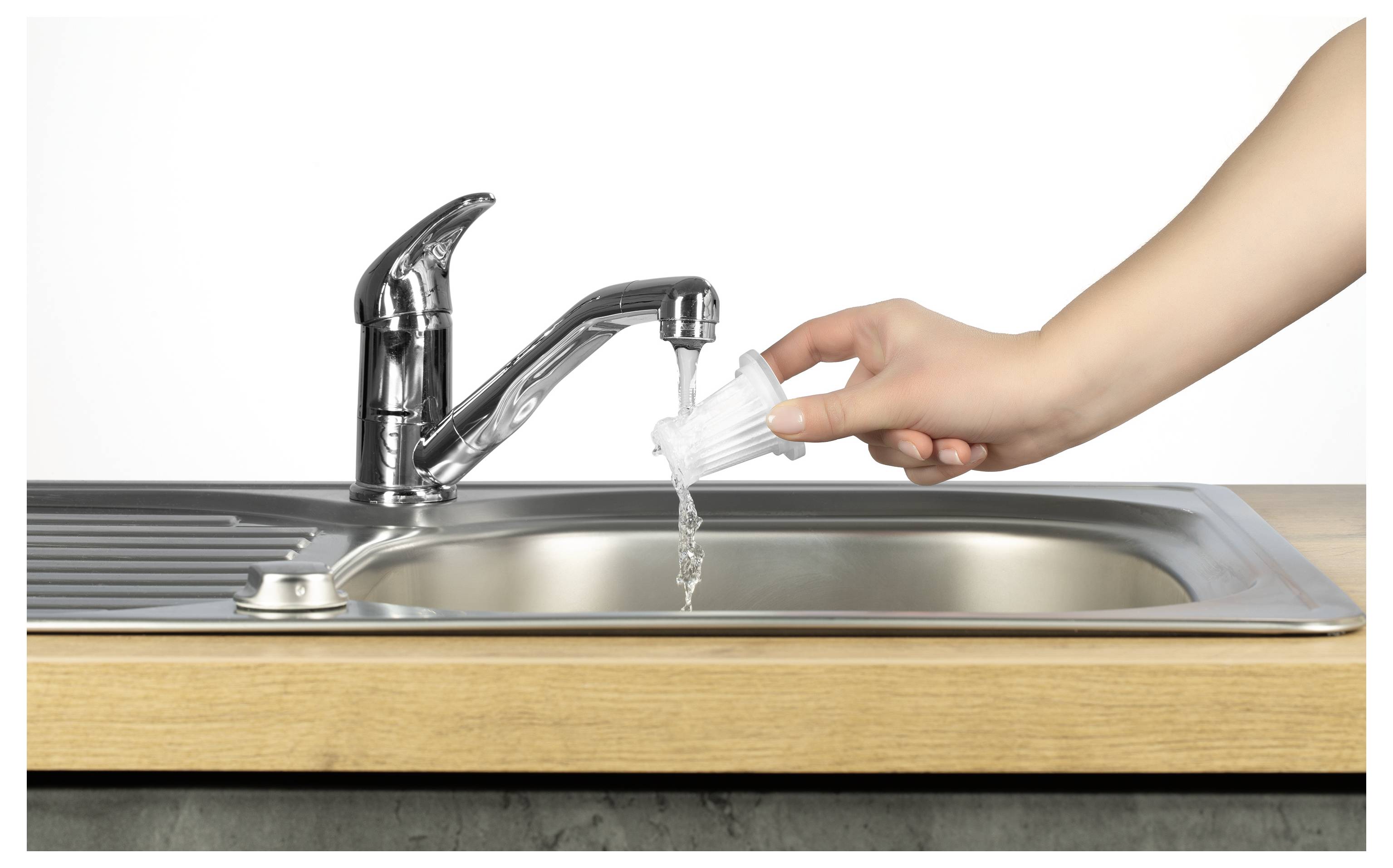 Eine Hand spült ein weißes Objekt unter einem Küchenarmatur mit fließendem Wasser über einem metallischen Spülbecken ab, das in einer Holzarbeitsplatte eingebaut ist.