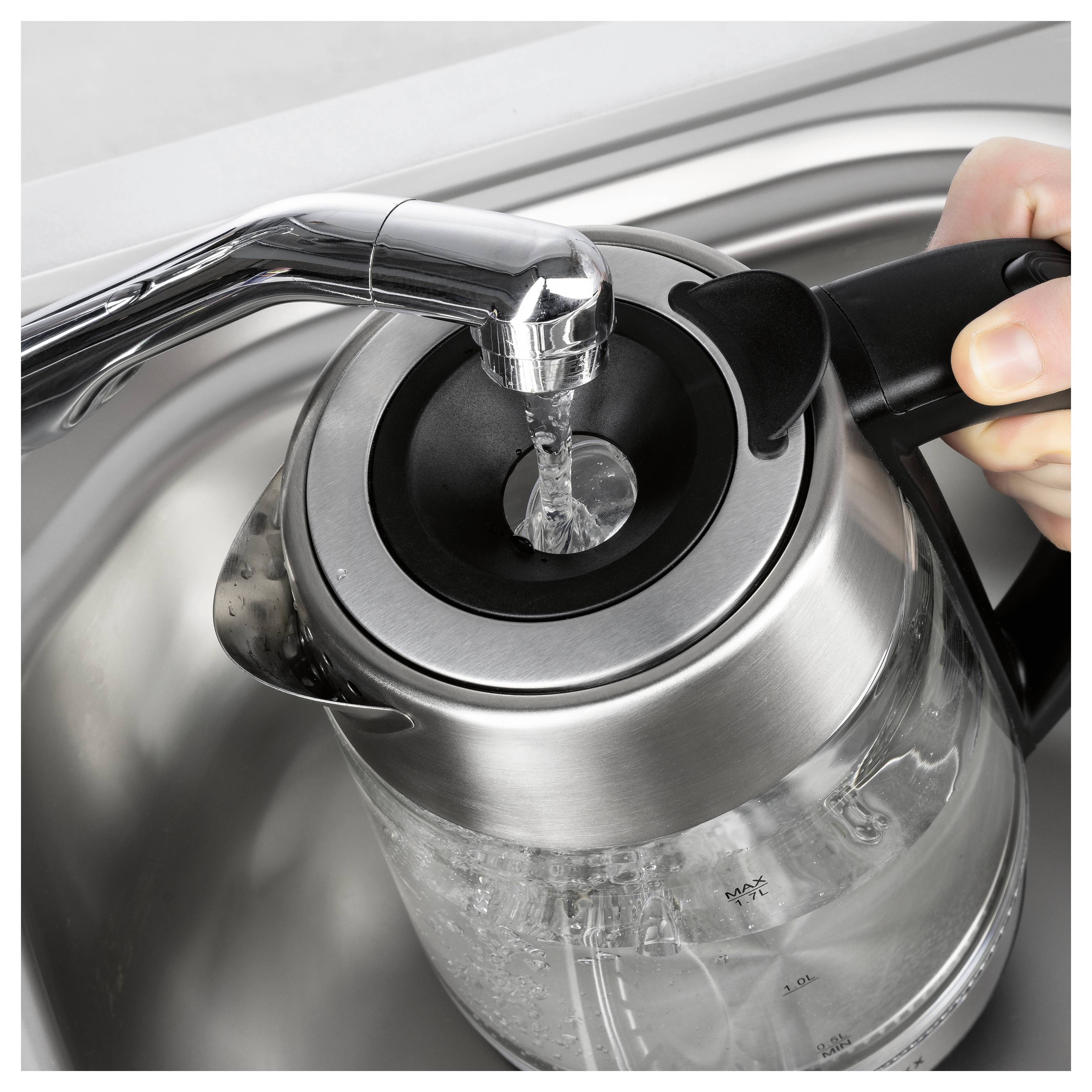 Das Füllen eines gläsernen elektrischen Wasserkochers mit Wasser aus einem Wasserhahn der Küche, wobei der Wasserkocher unter dem Wasserhahn in einem Metallspülbecken positioniert ist.