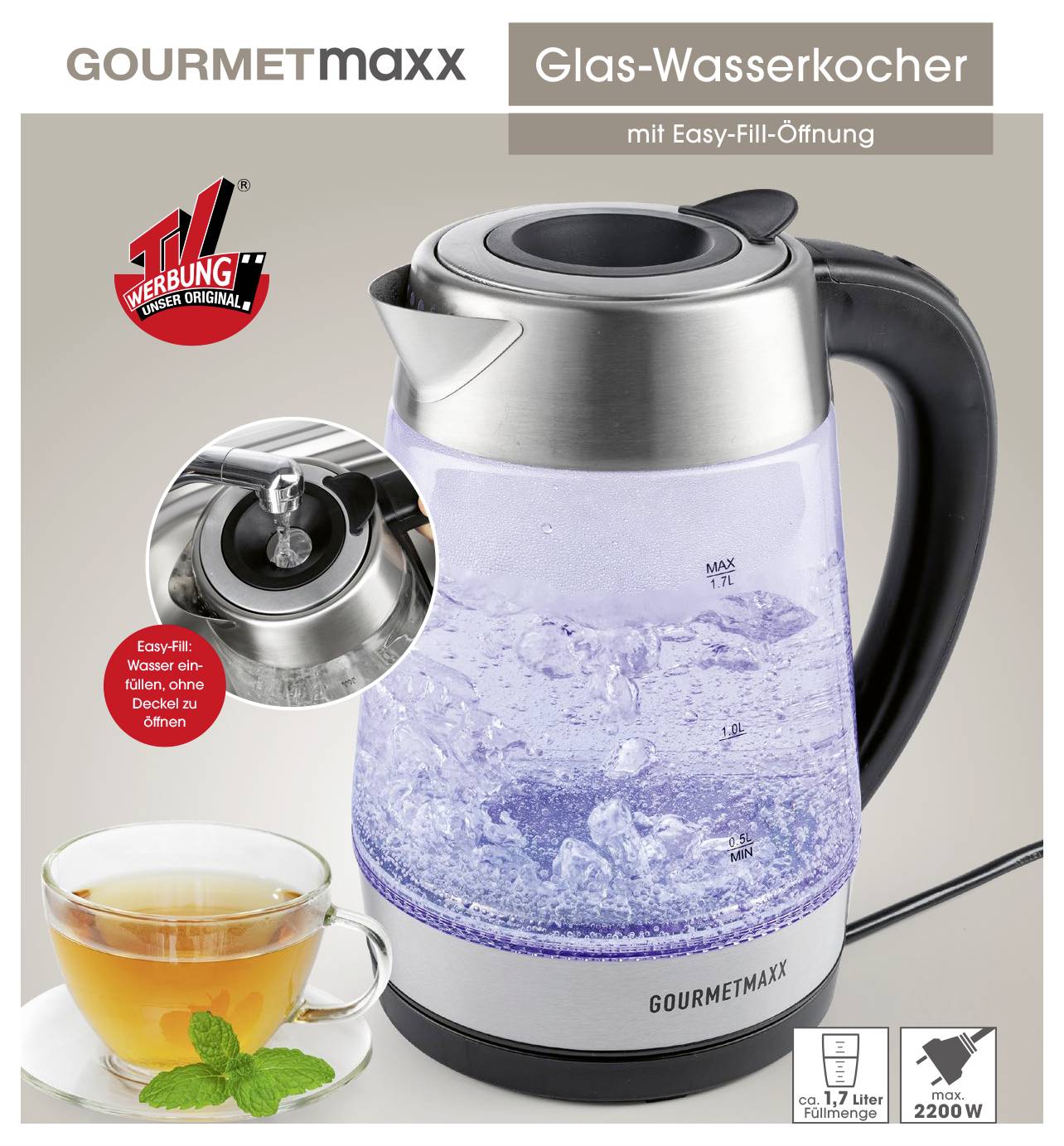Ein gläserner elektrischer Wasserkocher gefüllt mit kochendem Wasser neben einer Tasse Tee. 'GOURMETmaxx' Branding und 'Easy-Fill' Funktionstext sind sichtbar.